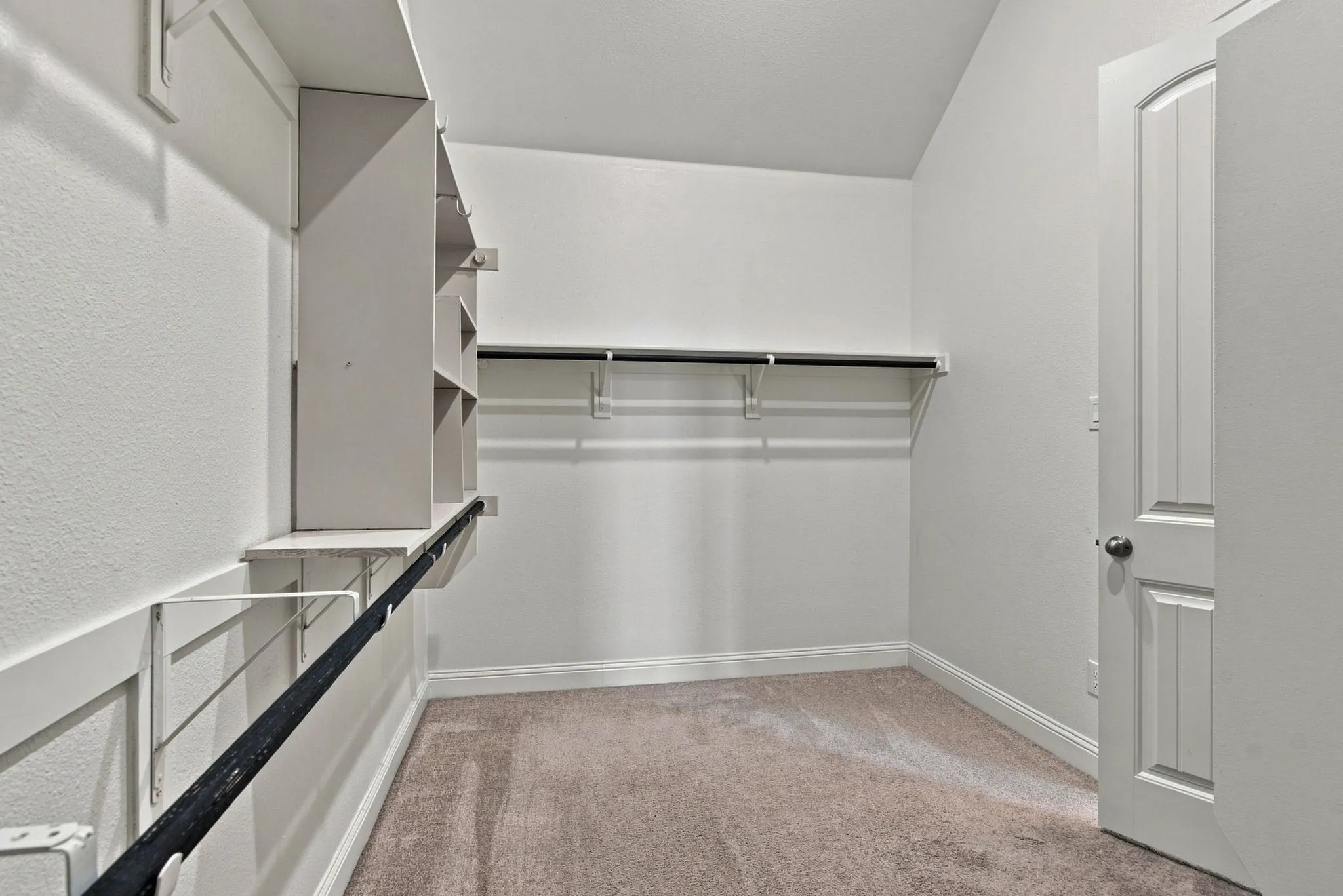 Walk-in closet featuring built-in shelving, multiple hanging rods, and neutral-toned carpeting