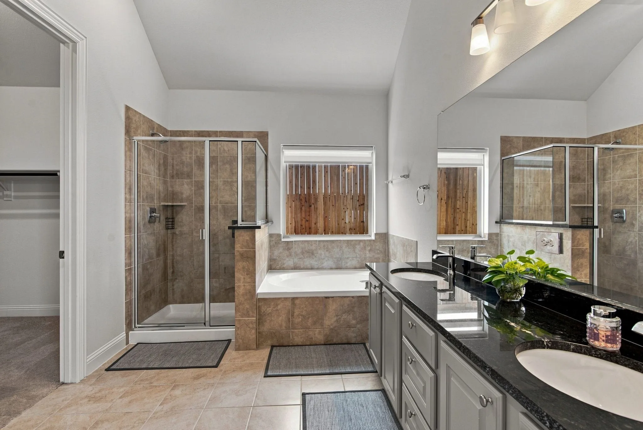 Bathroom featuring a dual vanity with granite countertops, a built-in tub, and a separate glass-enclosed shower