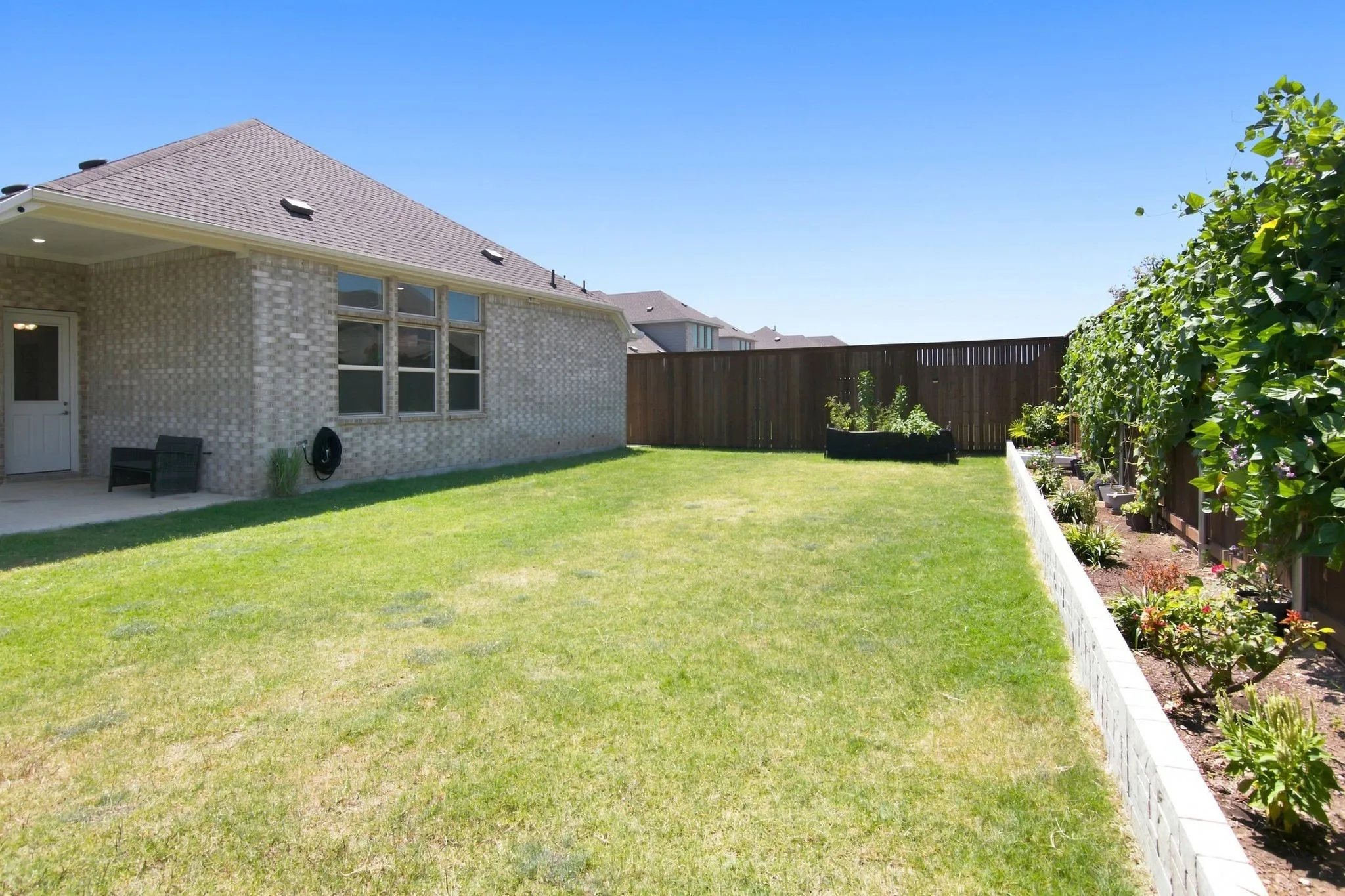 Expansive green lawn with a covered patio area, featuring a brick exterior and a privacy fence