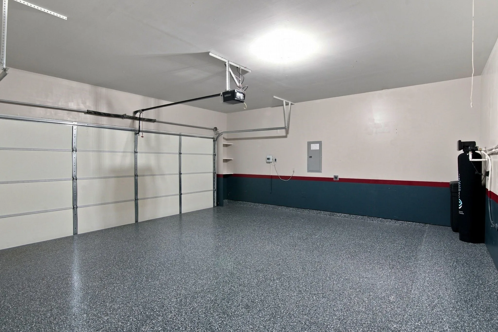 Spacious garage featuring a finished epoxy floor, white paneled overhead door, automatic opener, and overhead lighting