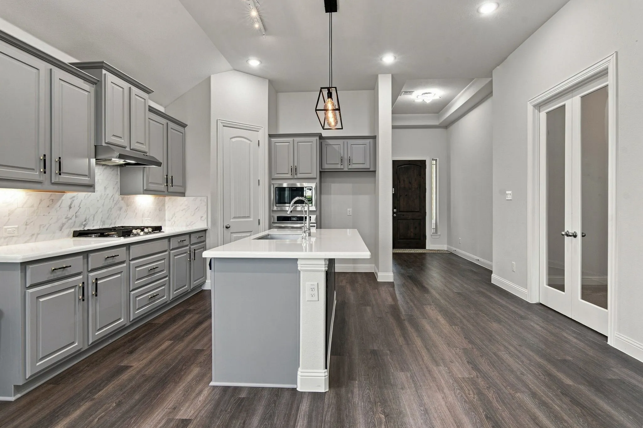 Open-concept kitchen featuring an island with a white countertop, gray cabinetry with dark hardware, a gas cooktop, and wood-finish flooring