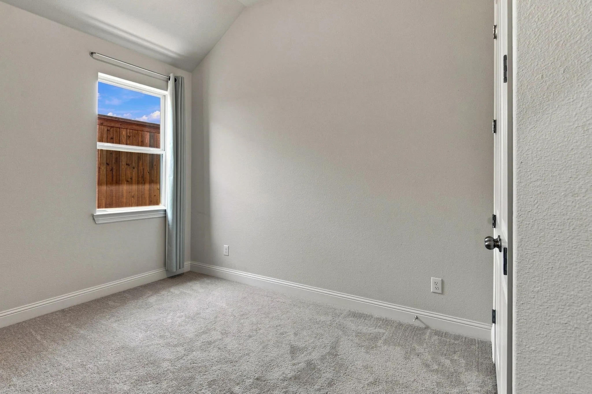 Carpeted room featuring a single window with white trim, a wood fence visible outside, and a white door with dark hardware