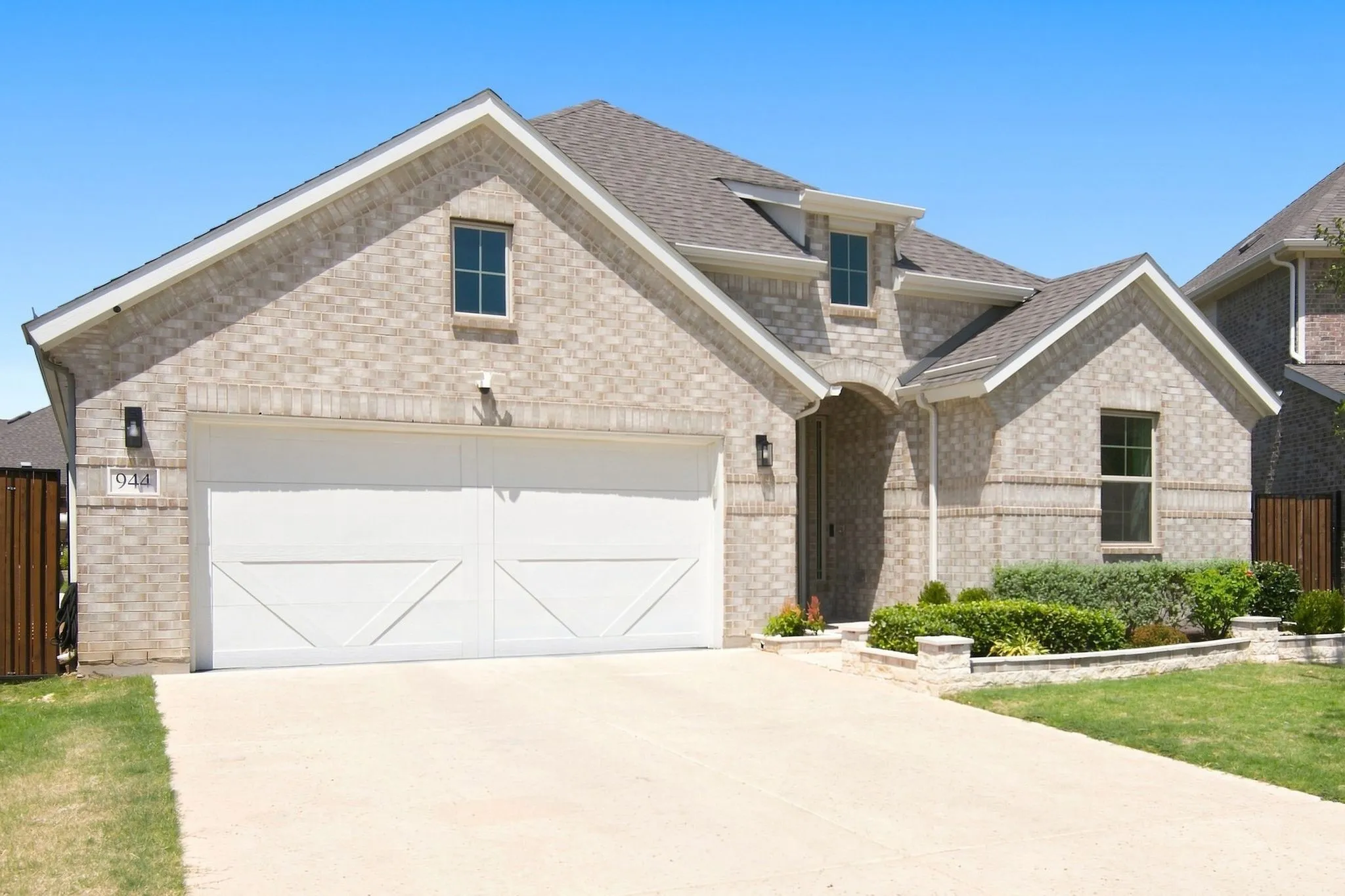 Contemporary brick exterior with a two-car garage, dormer windows, landscaped front yard, and a paved driveway