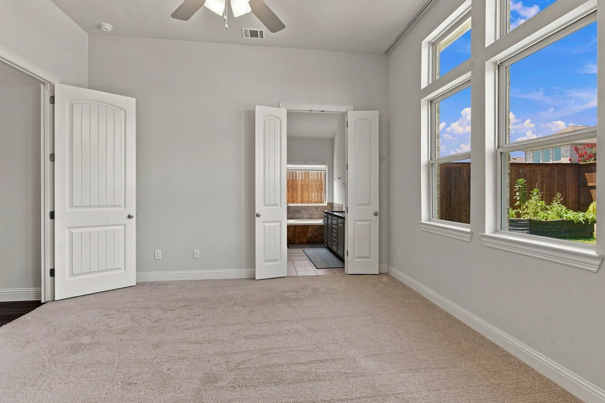 Carpeted room featuring large windows, vaulted ceiling, and an integrated ceiling fan