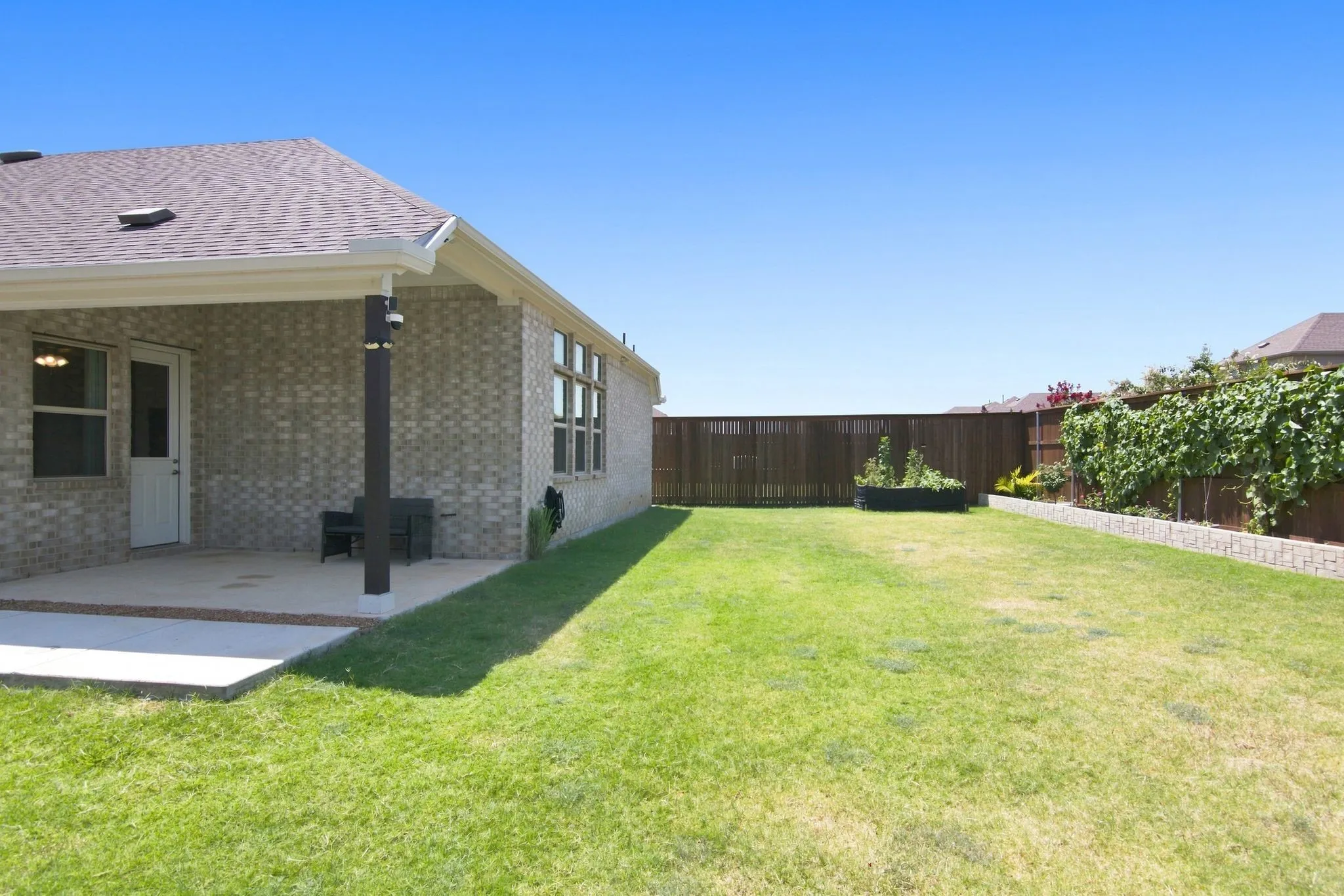 Expansive backyard featuring a concrete patio, a privacy fence, and a raised garden bed