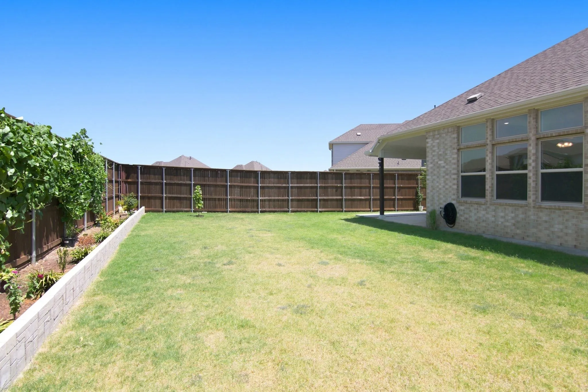 Spacious backyard featuring a substantial lawn, perimeter privacy fencing, and a concrete retaining wall bordering a cultivated garden bed with established plantings