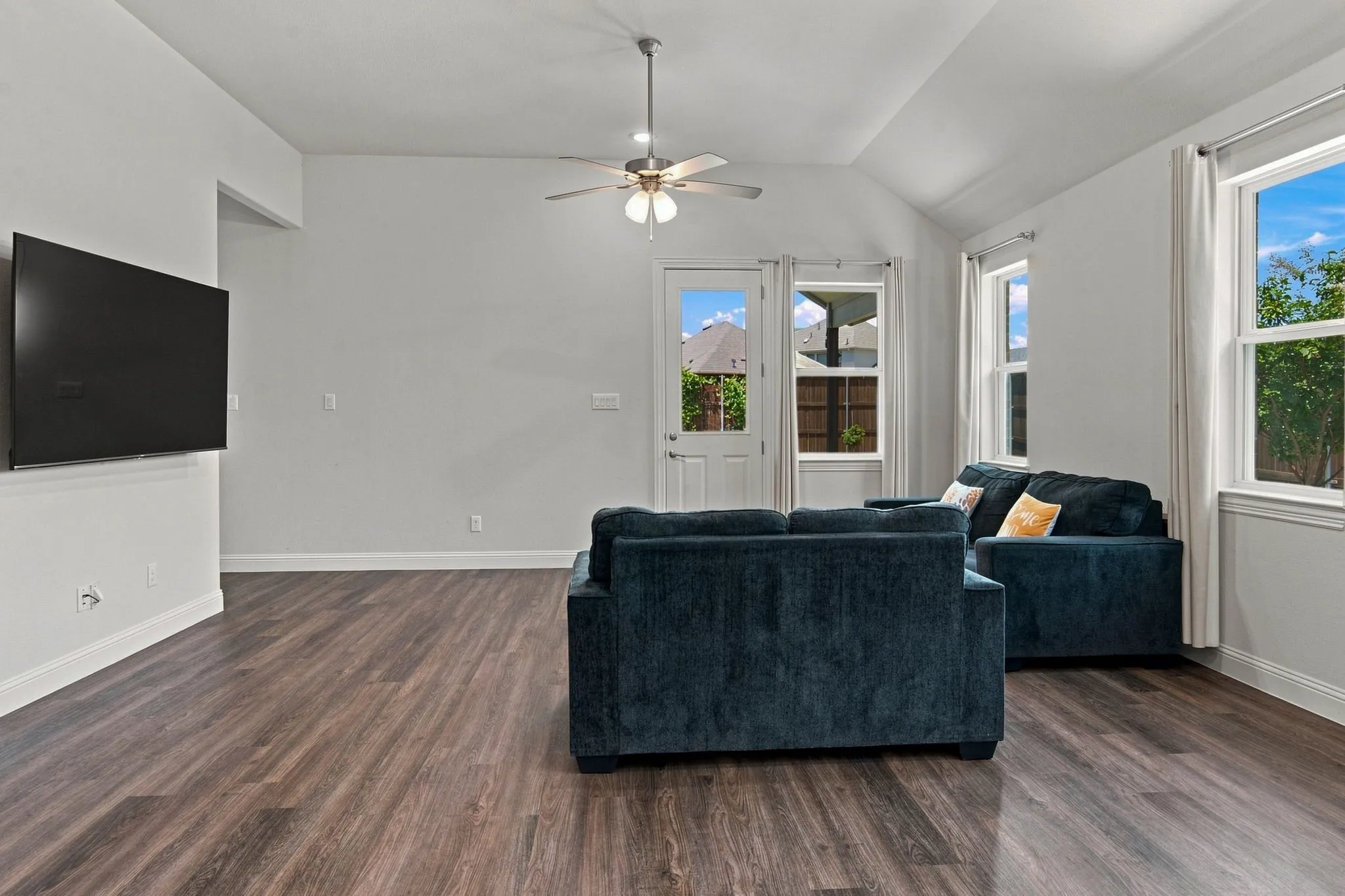 Spacious living area featuring wood-finish flooring, vaulted ceilings, and a ceiling fan with integrated lighting