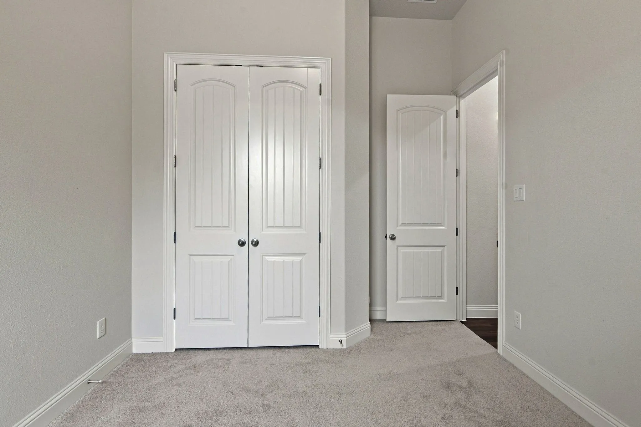 Room featuring a pair of white paneled bifold doors with chrome hardware, light gray carpeting, and white baseboards