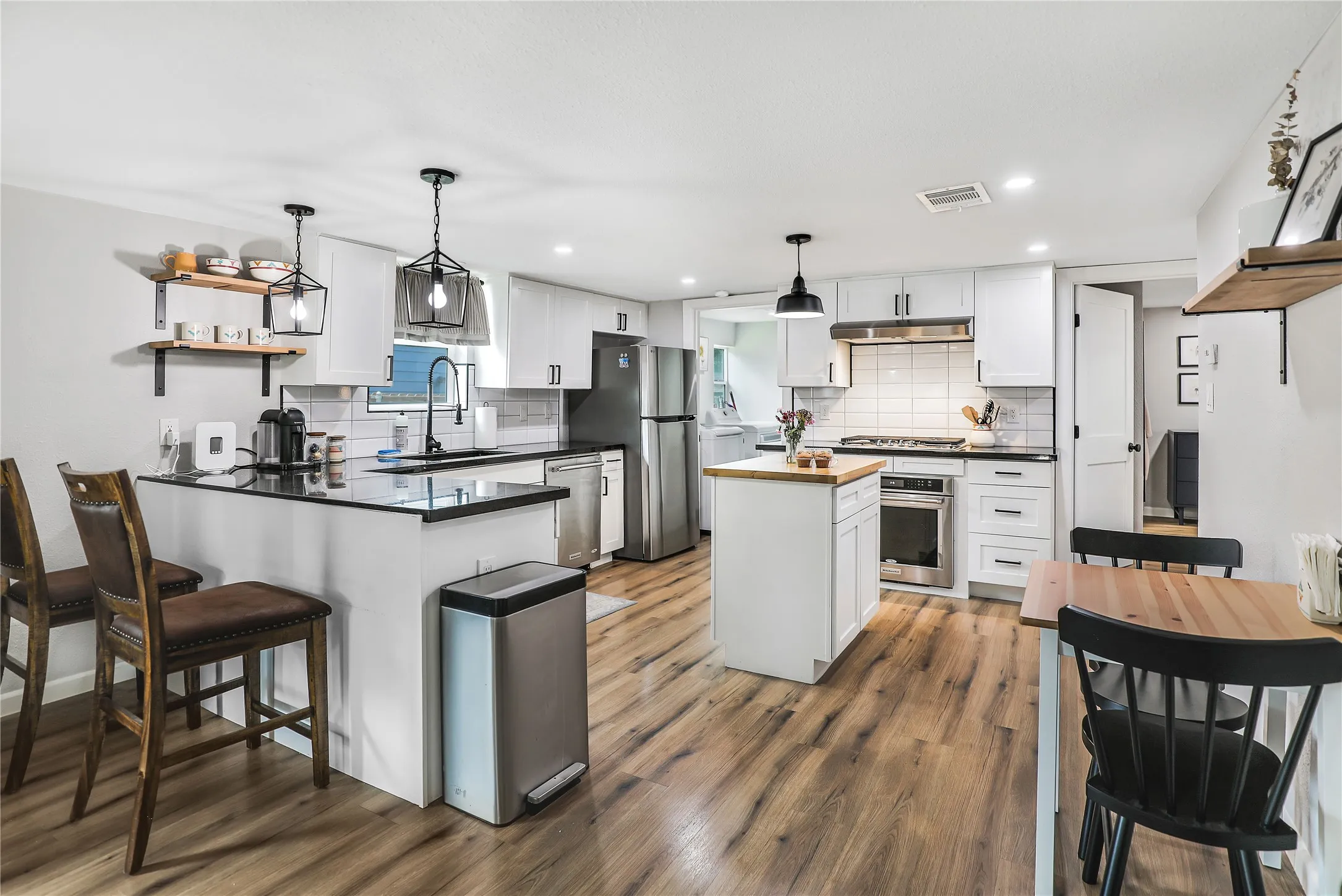 Open-concept kitchen featuring white cabinetry, black countertops, and stainless steel appliances