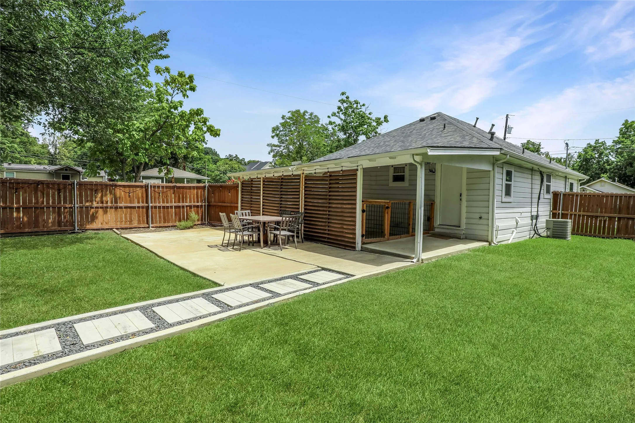 Expansive backyard featuring a covered patio with a slatted privacy wall, a concrete entertaining area, and a modern paver pathway set in gravel
