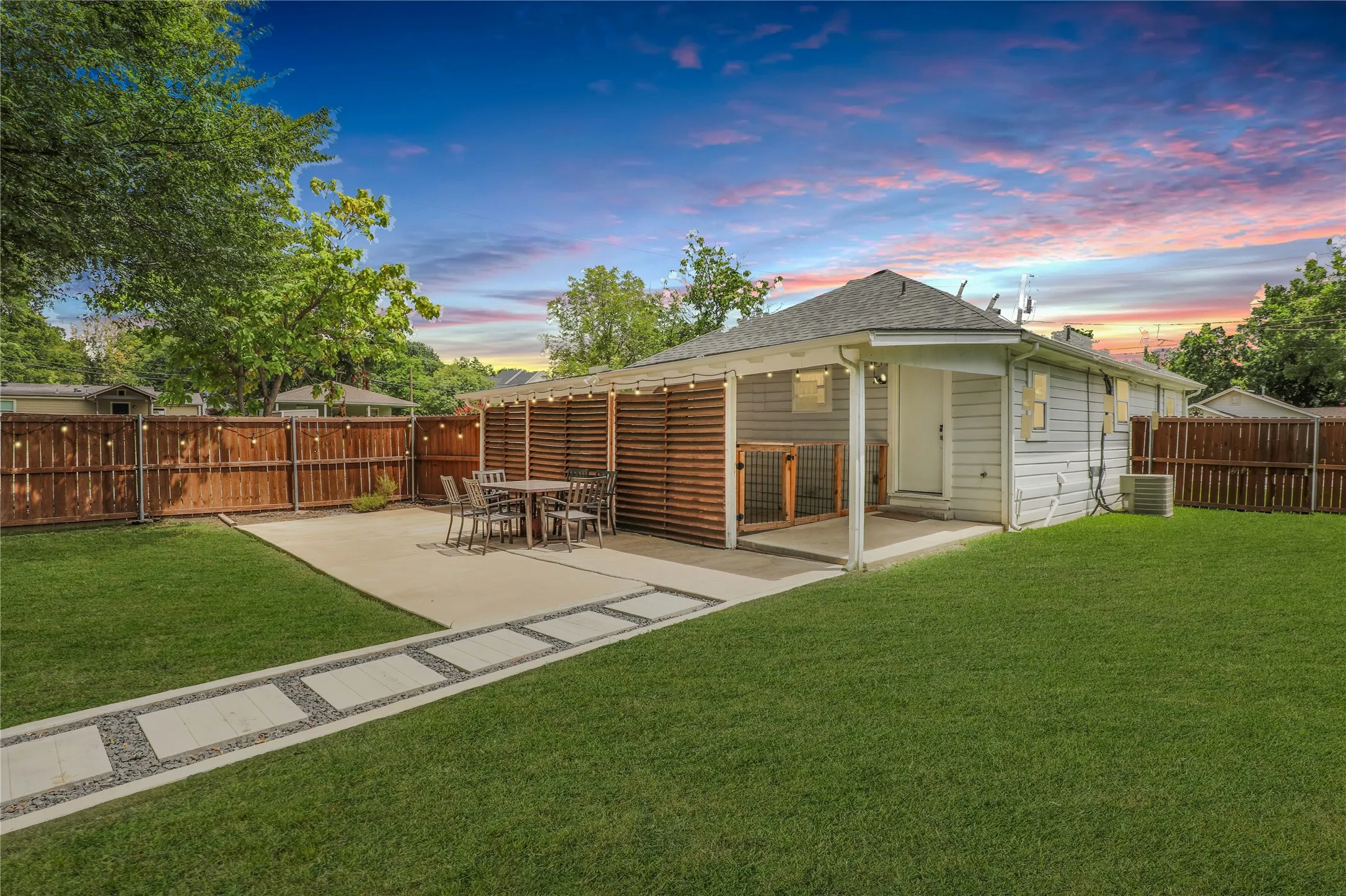 Expansive backyard featuring a concrete patio with slatted wood privacy screens, a covered porch, established green lawn, and a pebble-inlaid stepping stone path