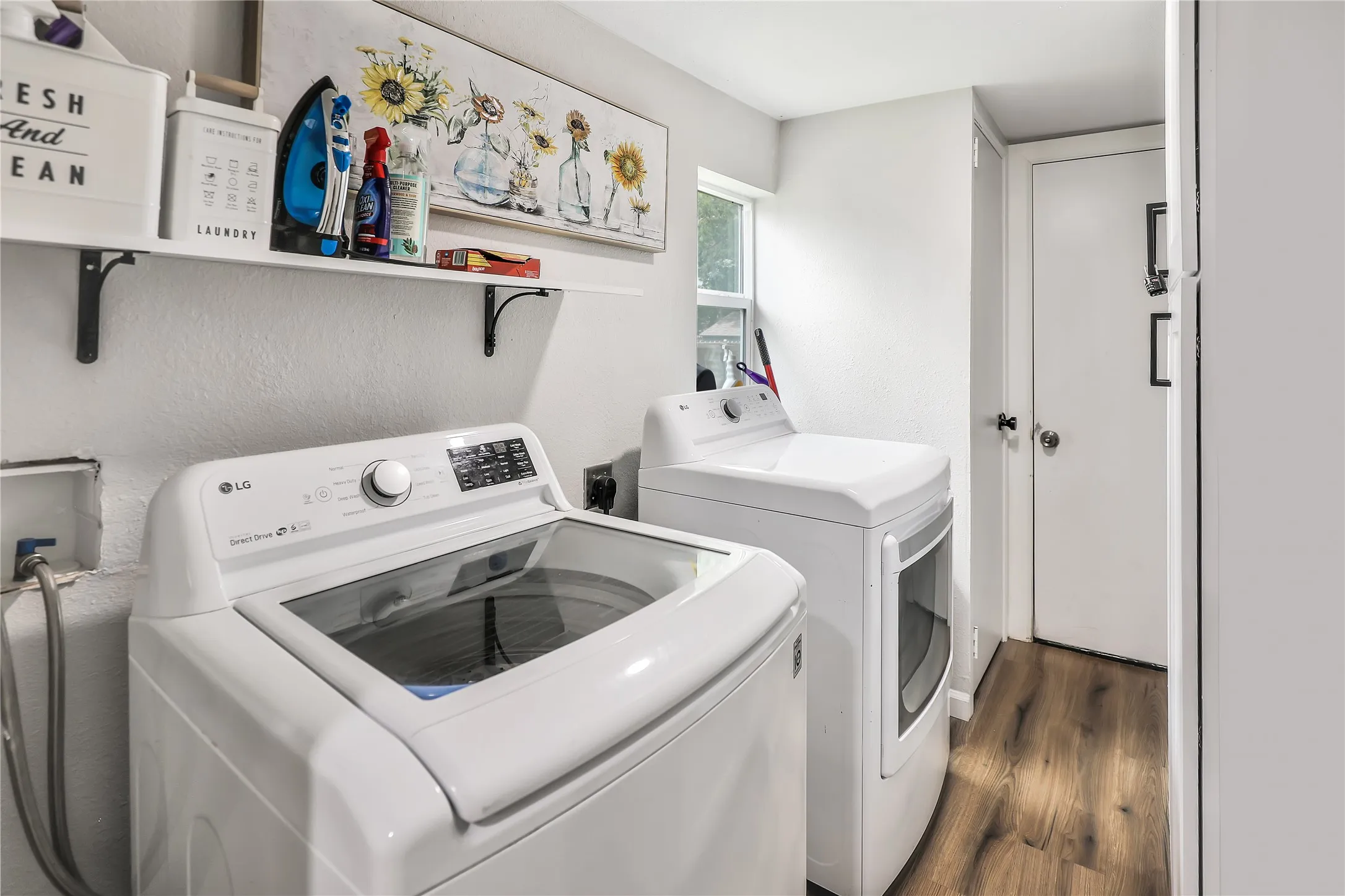 Dedicated laundry area featuring wood-finish flooring, white walls, and a white wall-mounted shelving unit