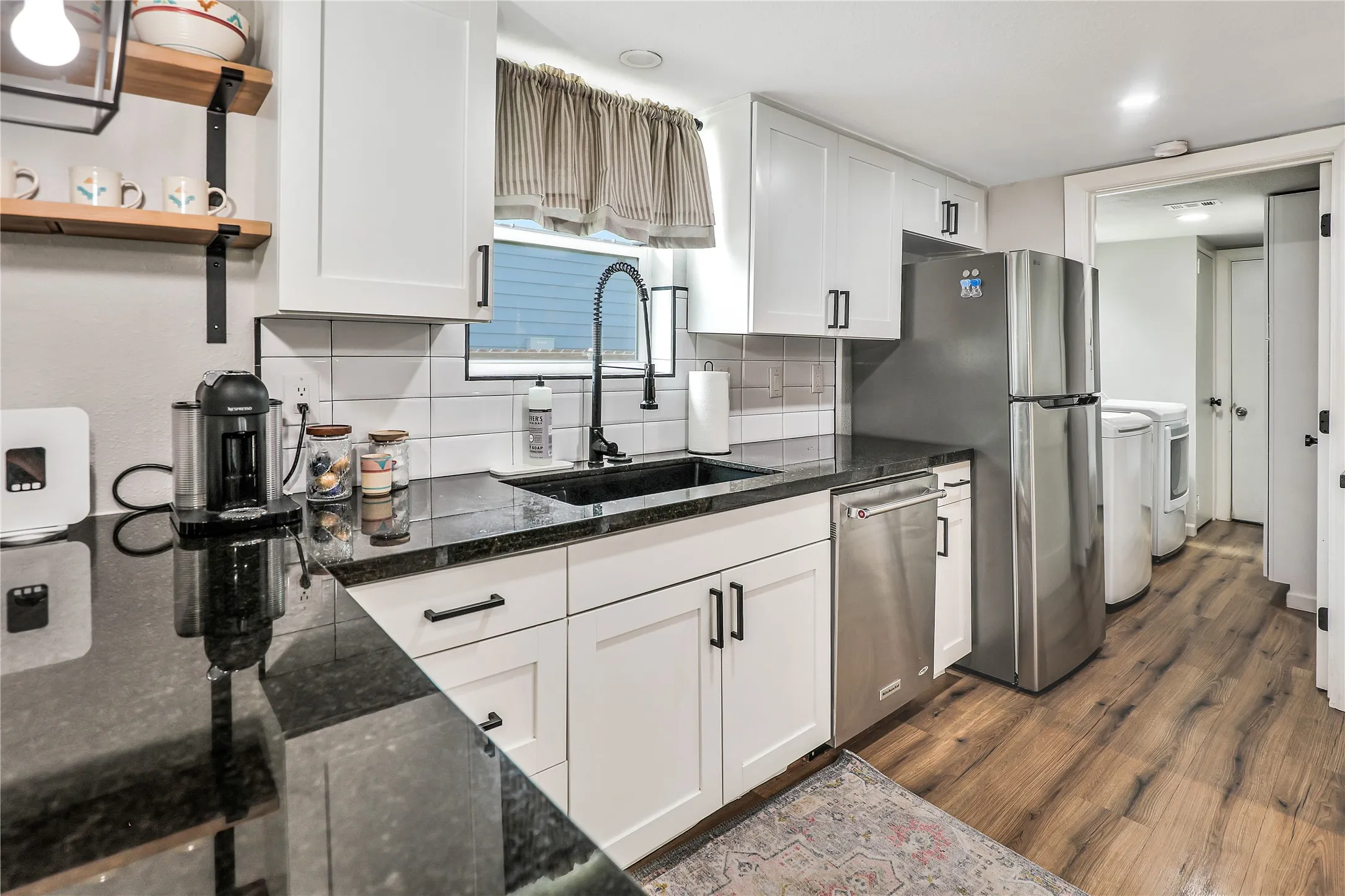 Contemporary kitchen featuring white cabinetry with black hardware, dark countertops, white subway tile backsplash, and stainless steel appliances