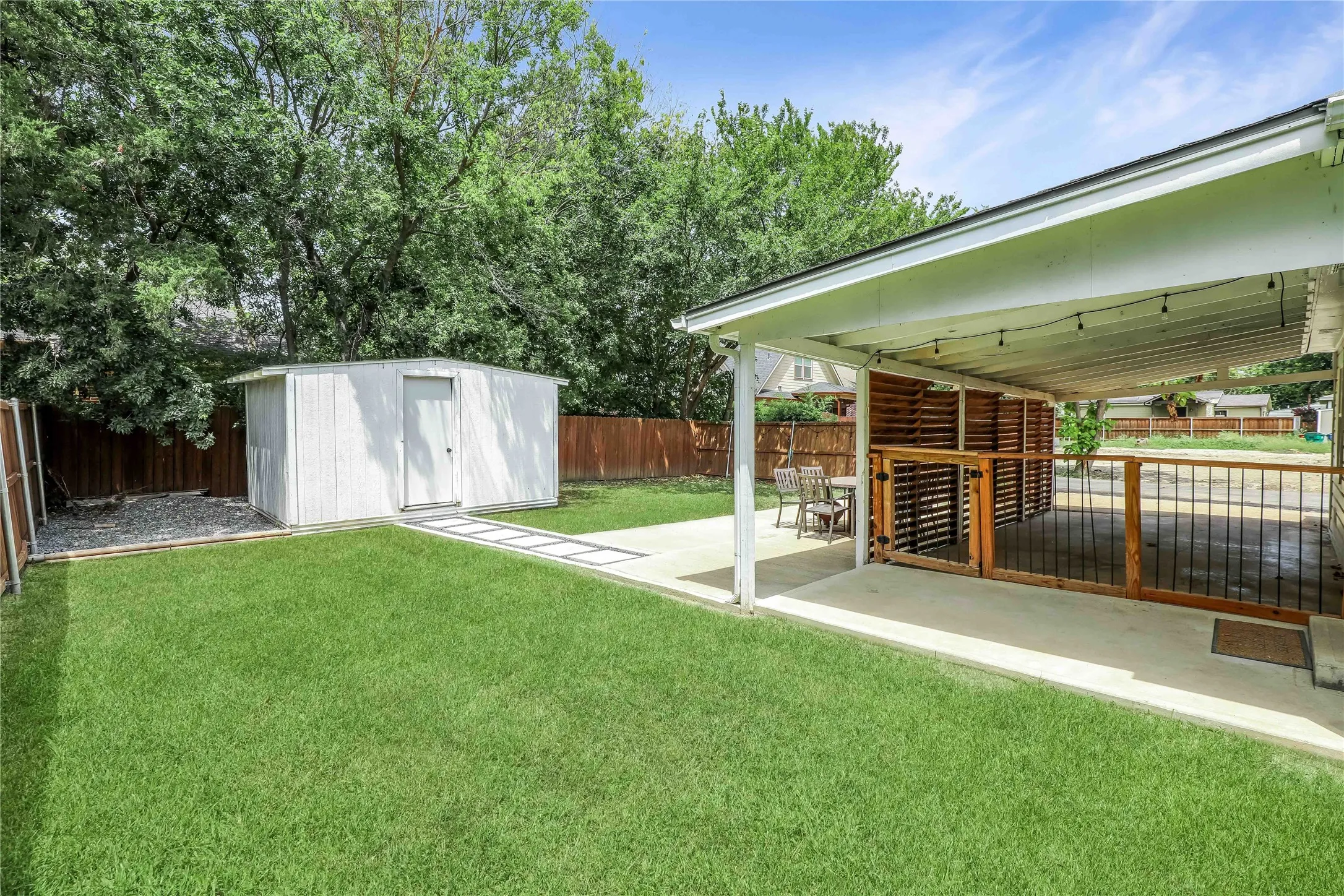 Expansive backyard featuring a covered patio with slatted wood screening, a separate storage shed, concrete patio flooring, and a manicured lawn