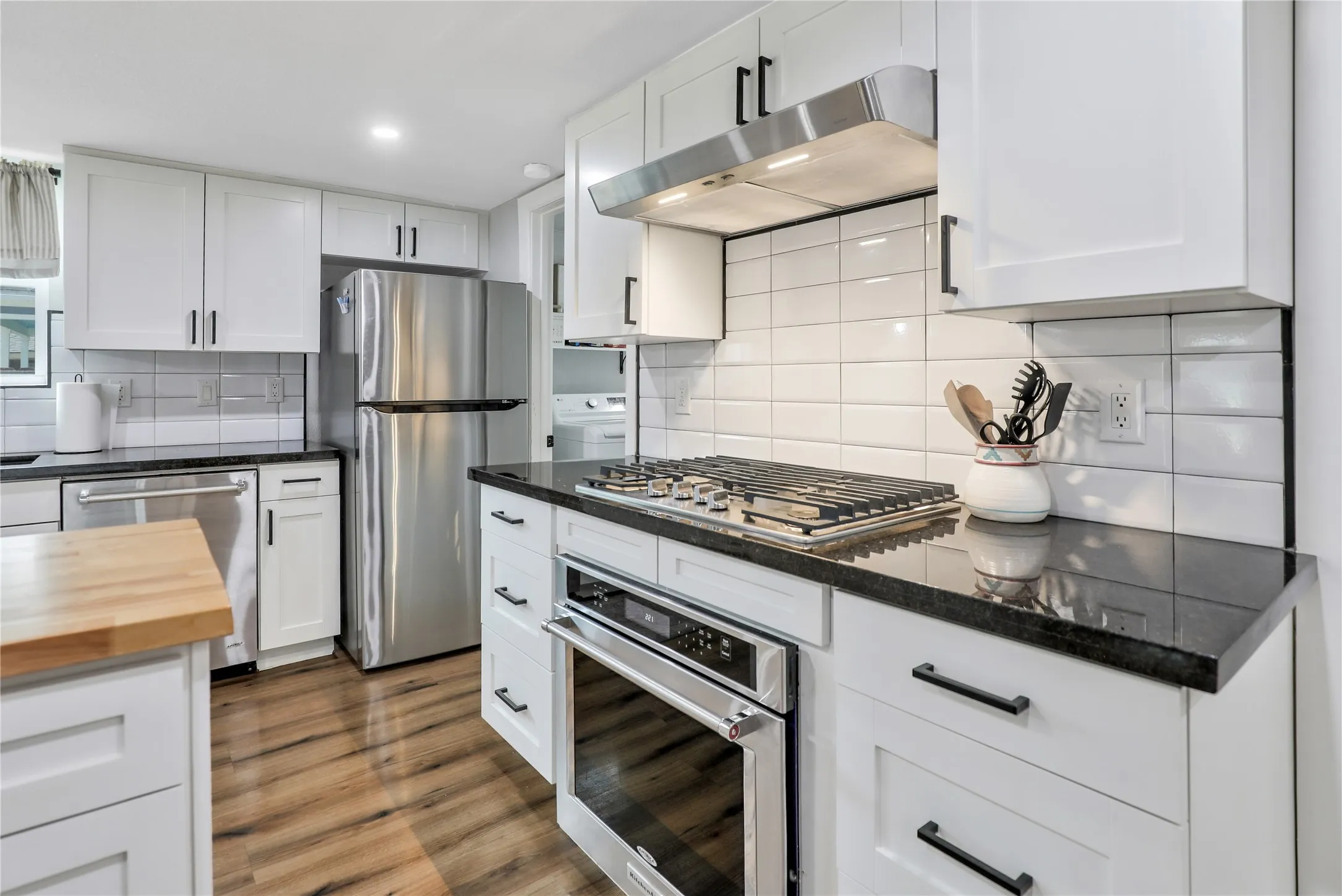 Modern kitchen featuring white shaker cabinetry, stainless steel appliances, dark countertops, a subway tile backsplash, and wood-finish flooring