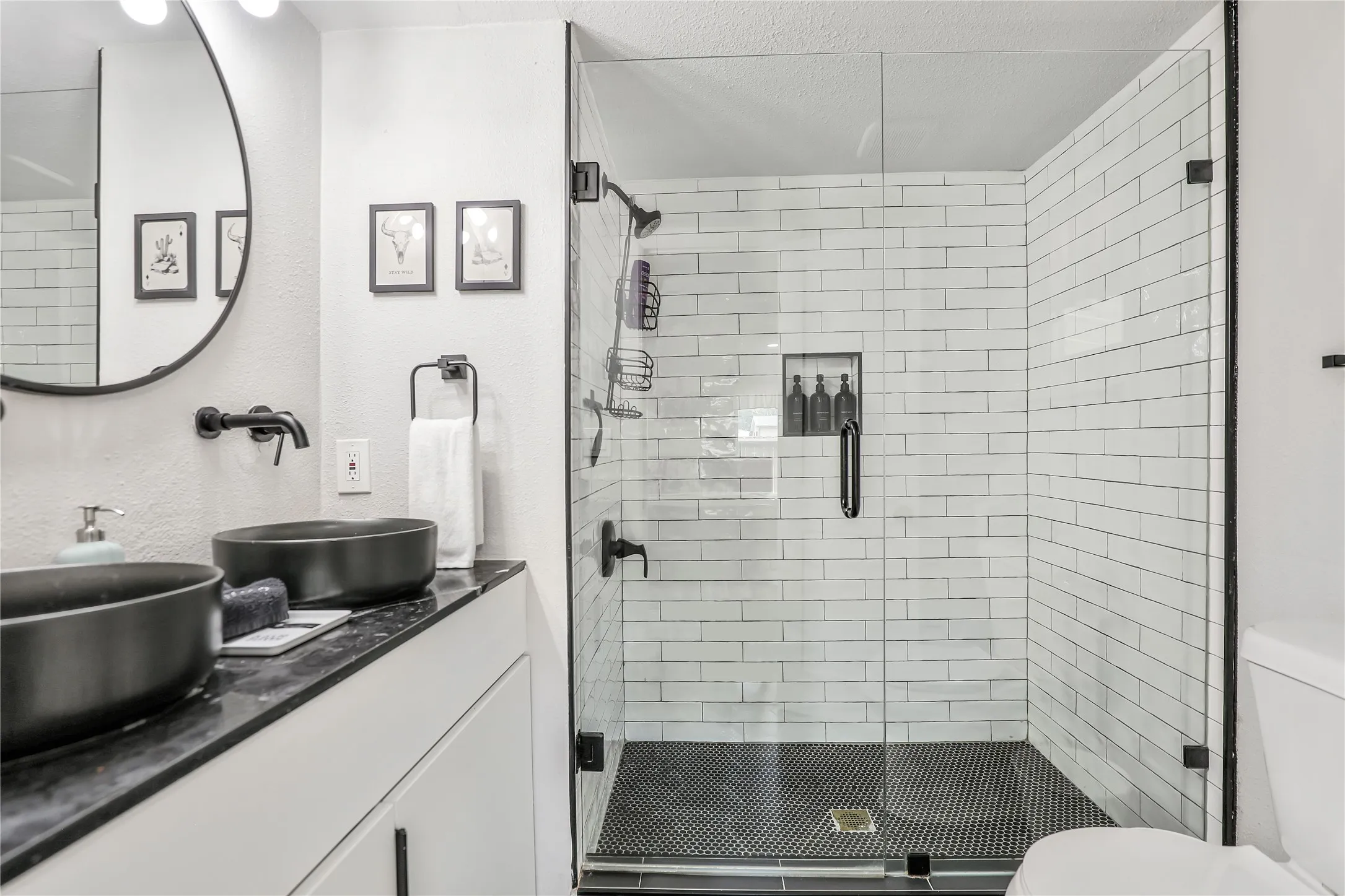 Bathroom featuring a glass-enclosed shower with subway tile surround and black penny tile floor