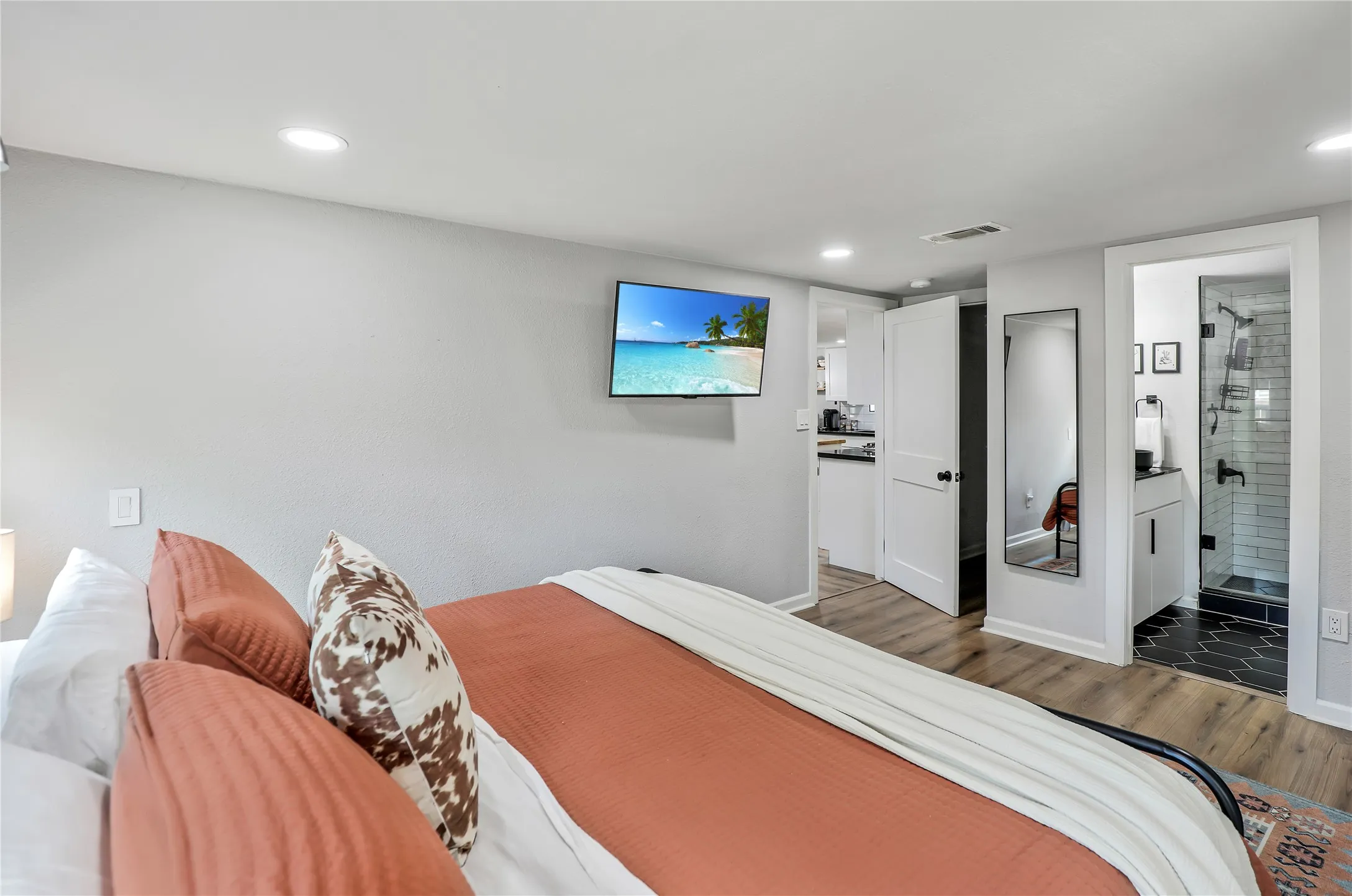 Recessed lighting illuminates a space featuring wood-finish flooring and a wall-mounted television