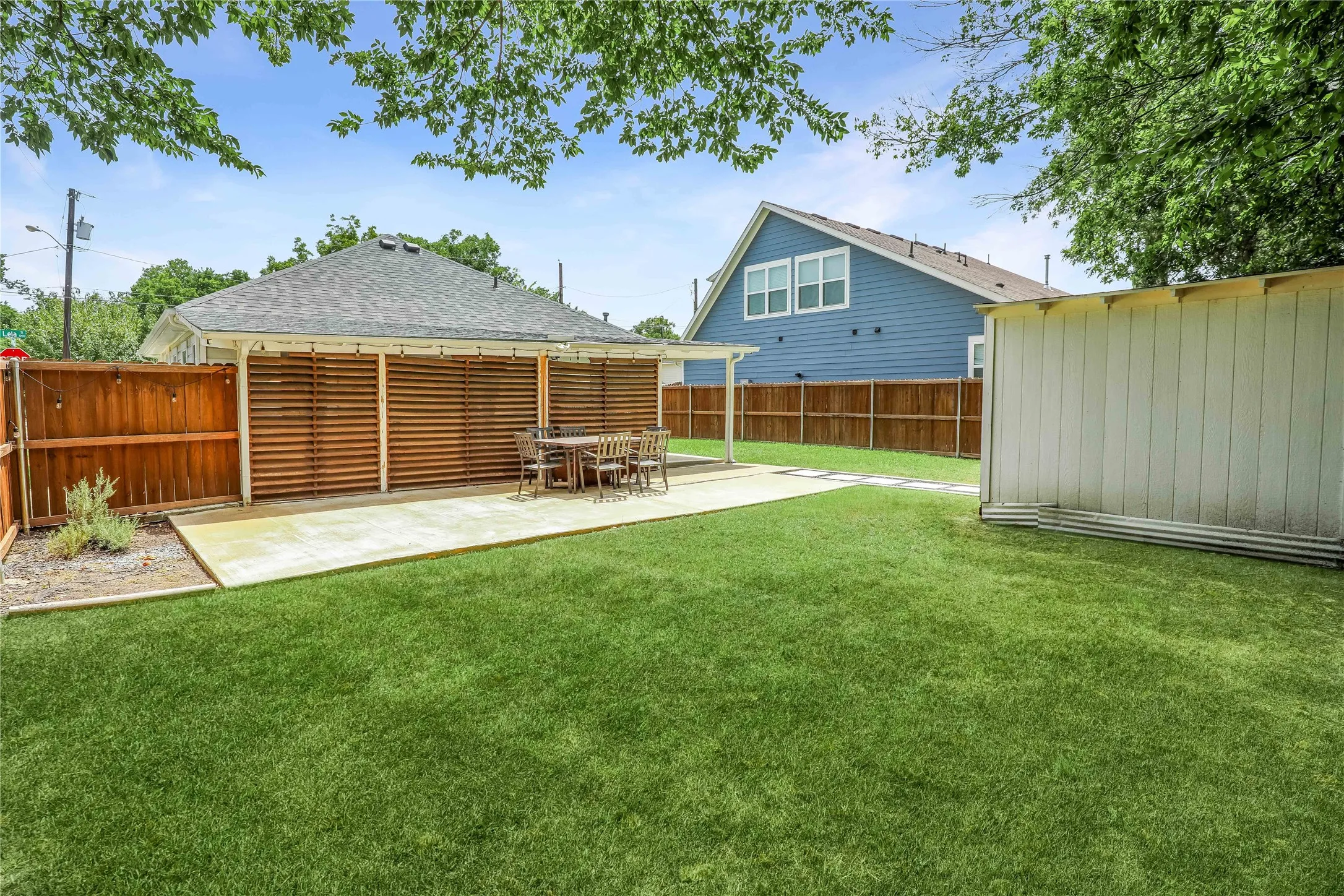 Expansive grass lawn featuring a concrete patio with a slatted privacy screen, a covered outdoor area, and wood fencing