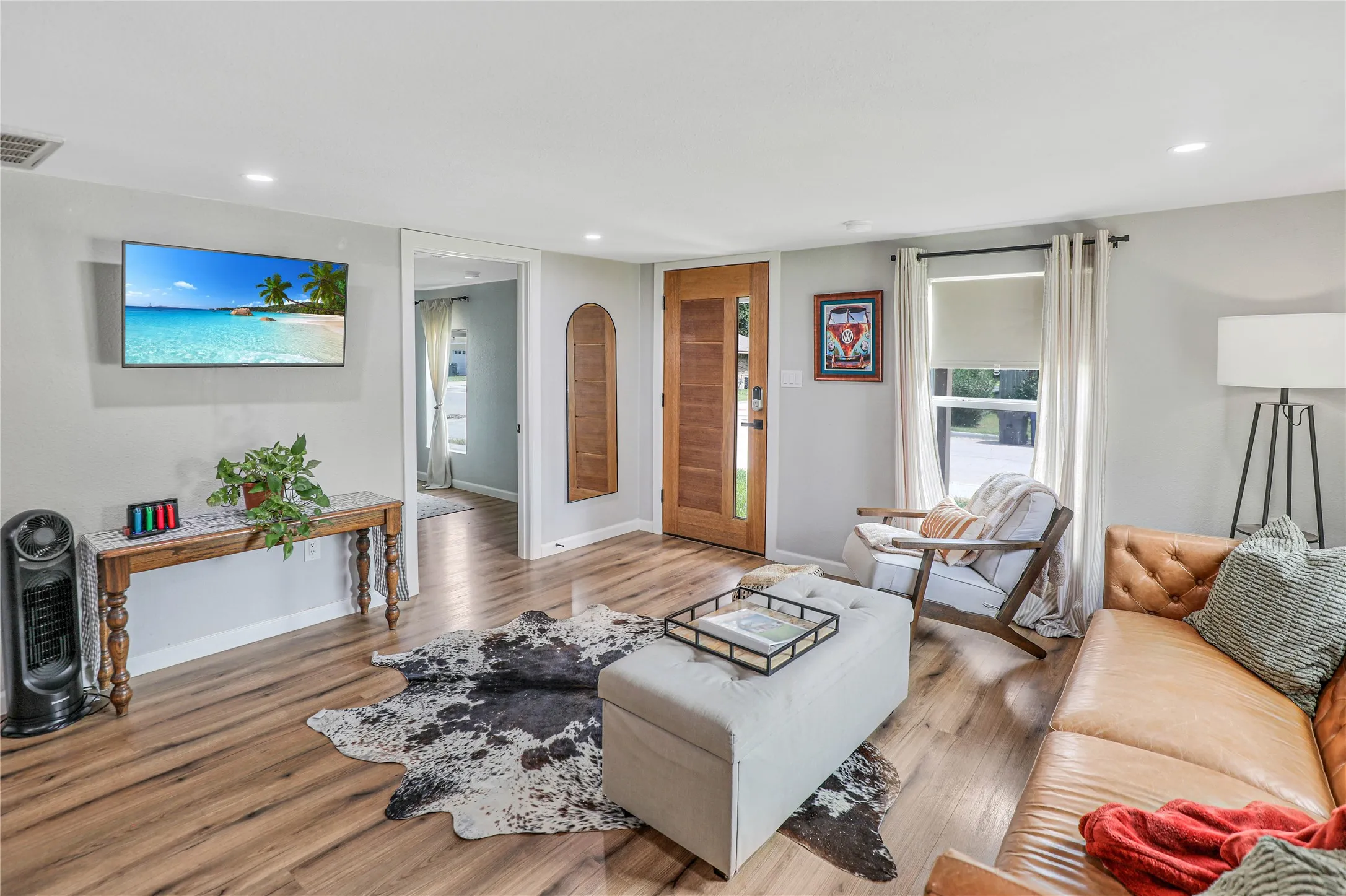 Bright living area featuring wood-finish flooring, recessed lighting, a wooden entry door with frosted glass, and a large window with roller shade