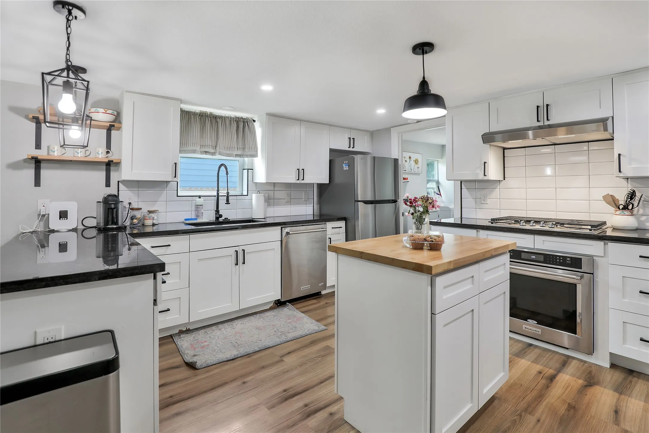 Kitchen featuring white shaker cabinetry, dark countertops, a central island with a wood-finish top, stainless steel appliances, and wood-finish flooring