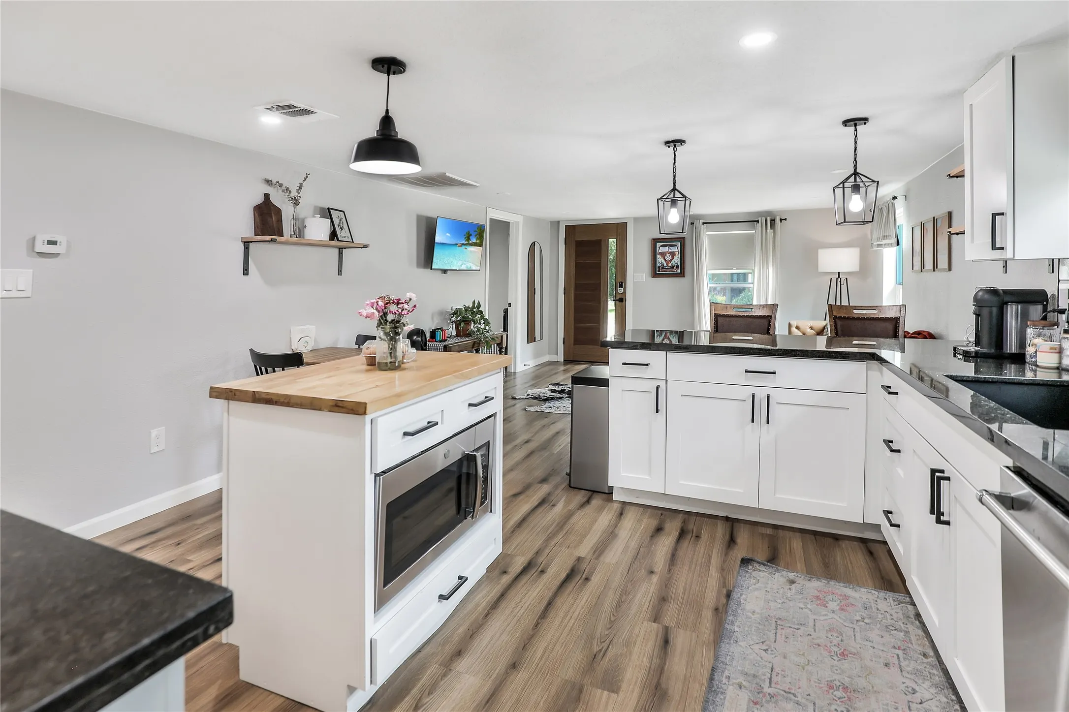 Kitchen featuring white cabinetry with black hardware, dark countertops, and wood-finish flooring