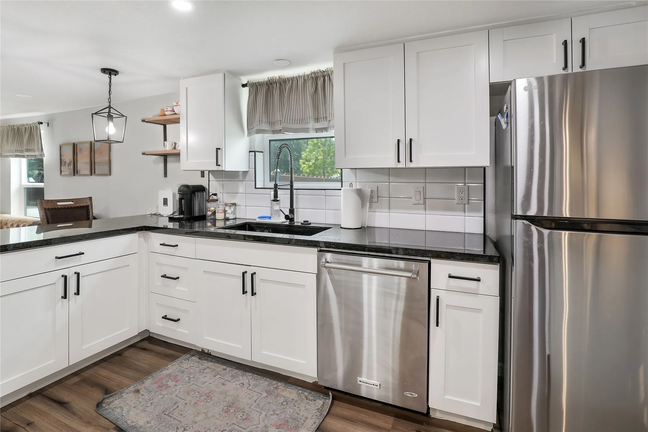 Modern kitchen featuring white shaker cabinetry, dark countertops, stainless steel appliances, and wood-finish flooring