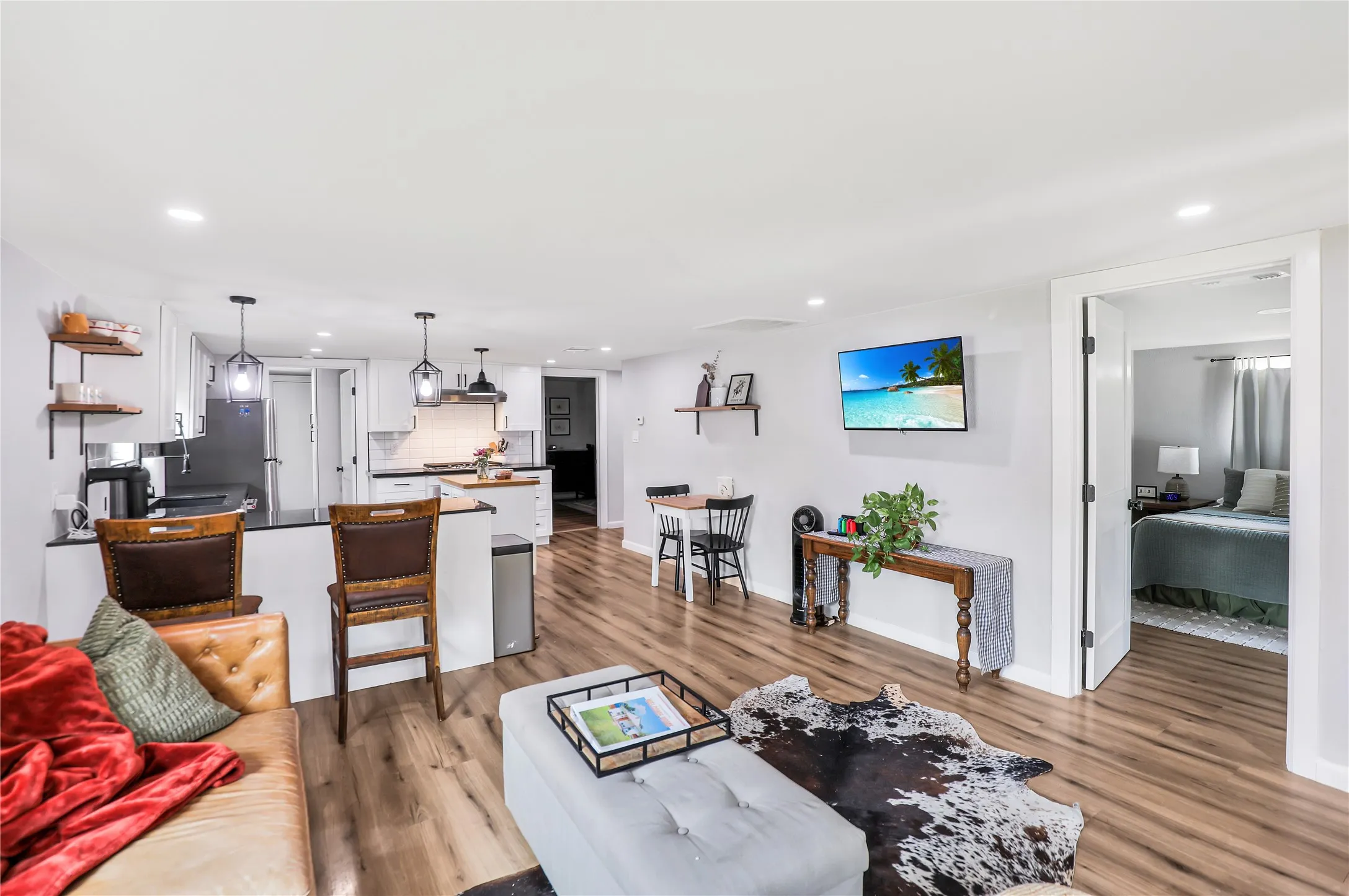 Spacious open-concept living area featuring wood-finish flooring, recessed lighting, and a kitchen with white cabinetry, black countertops, and pendant lighting