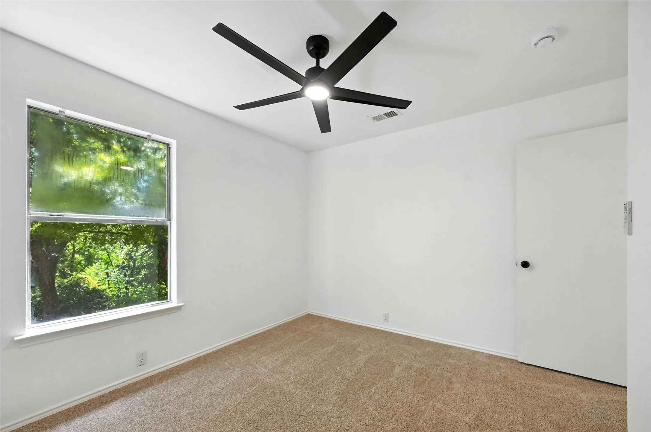 Carpeted empty room with ceiling fan and a smoke detector