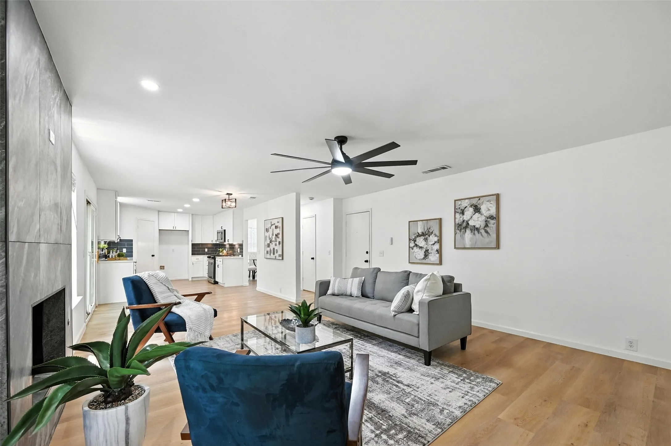 Living area with a ceiling fan, light wood-style flooring, a large fireplace, and recessed lighting
