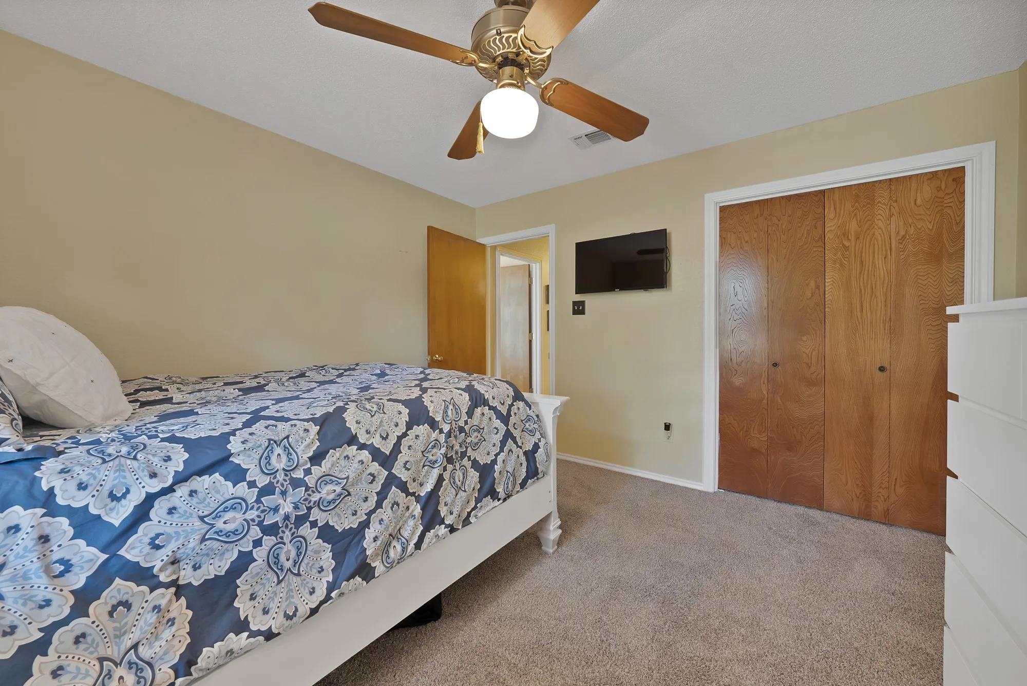 Plush carpeting, wood-finish bi-fold closet doors, and ceiling fan with integrated lighting