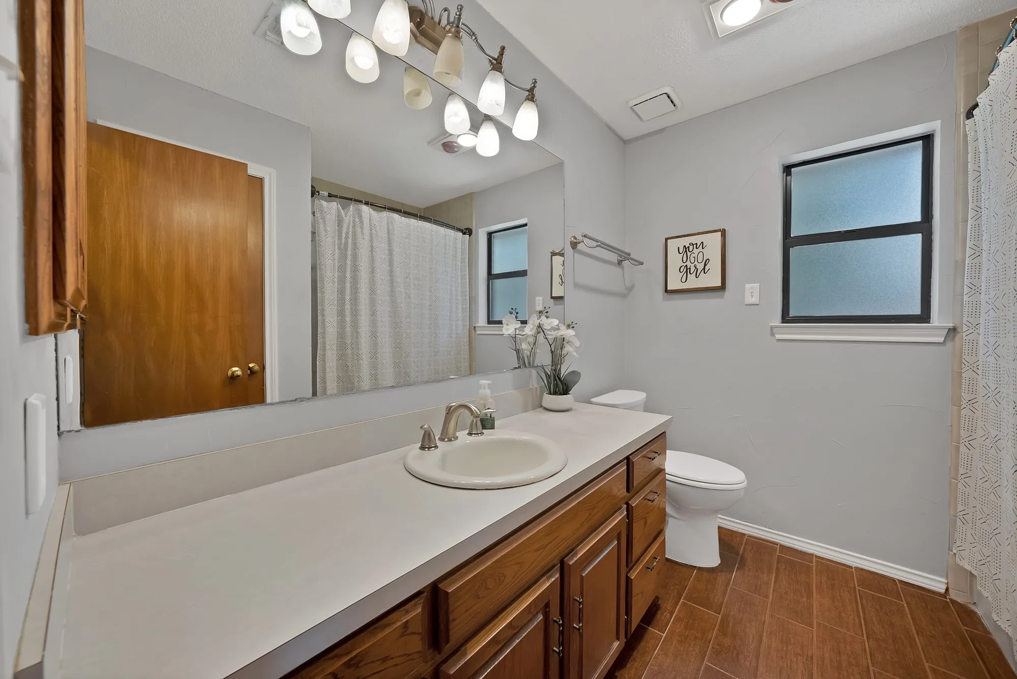 Wood-finish flooring, single vanity with integrated sink, wood cabinetry, privacy window, and wall-mounted light fixture