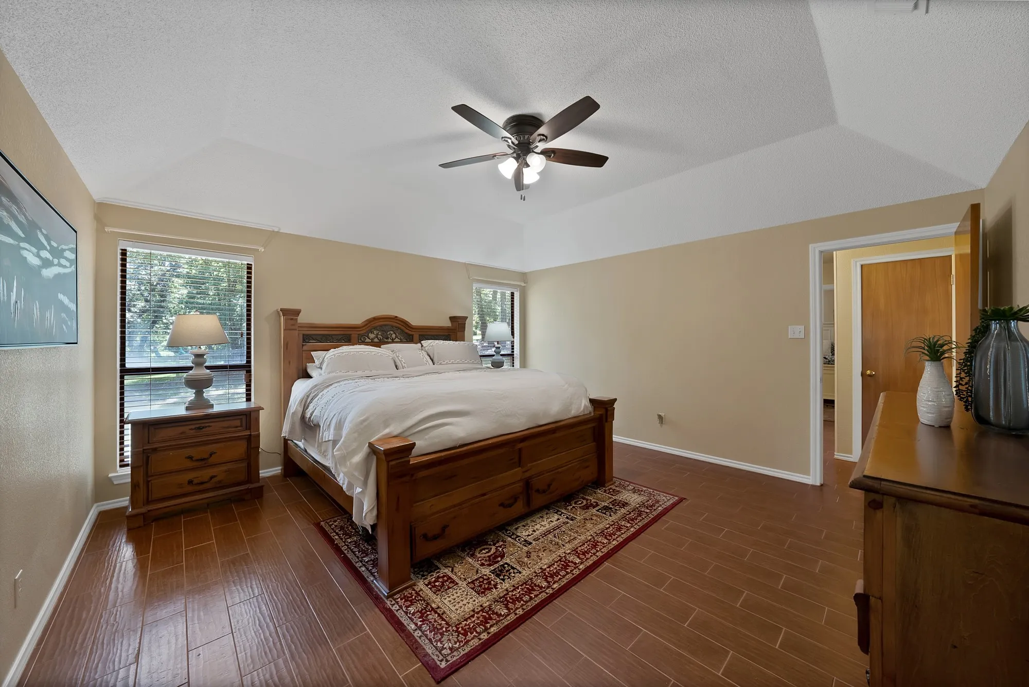 Vaulted ceiling with an integrated ceiling fan, wood-finish flooring, and multiple windows with blinds