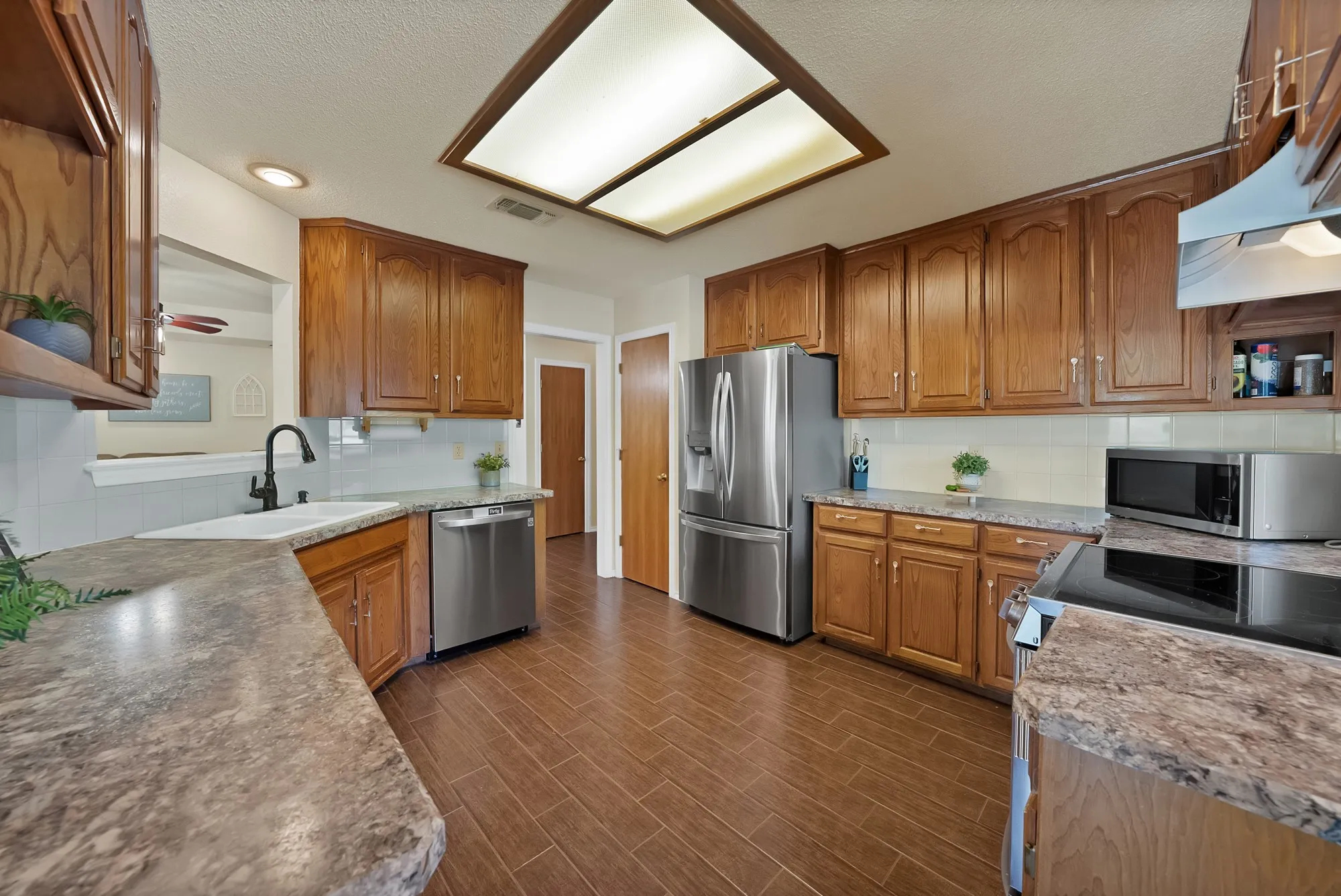 Kitchen featuring wood-finish cabinetry, stainless steel appliances, a white rectangular sink with a matte black faucet, wood-look flooring, and a recessed ceiling light panel
