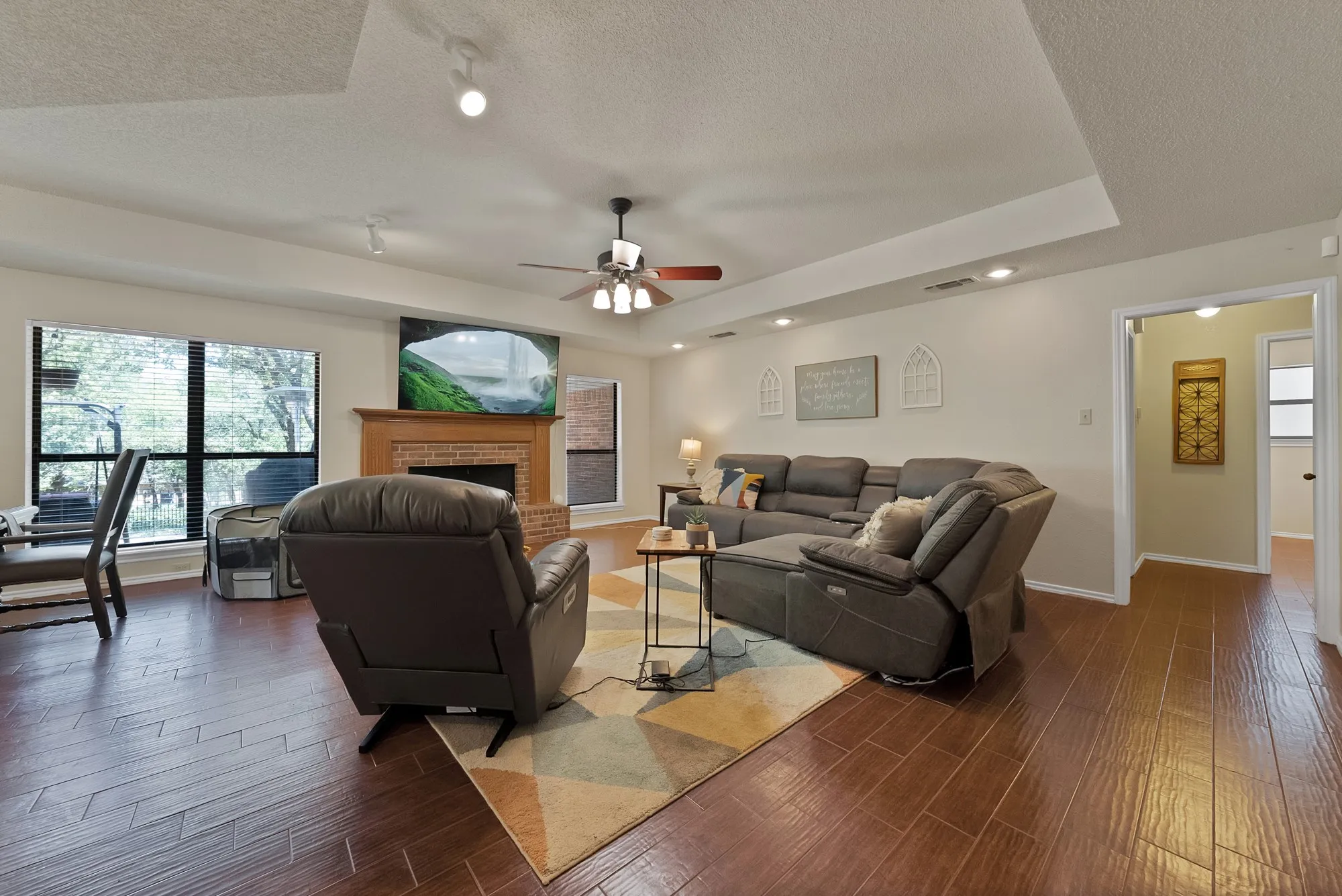 Spacious living area featuring wood-finish flooring, a brick fireplace with a wood mantel, and large windows
