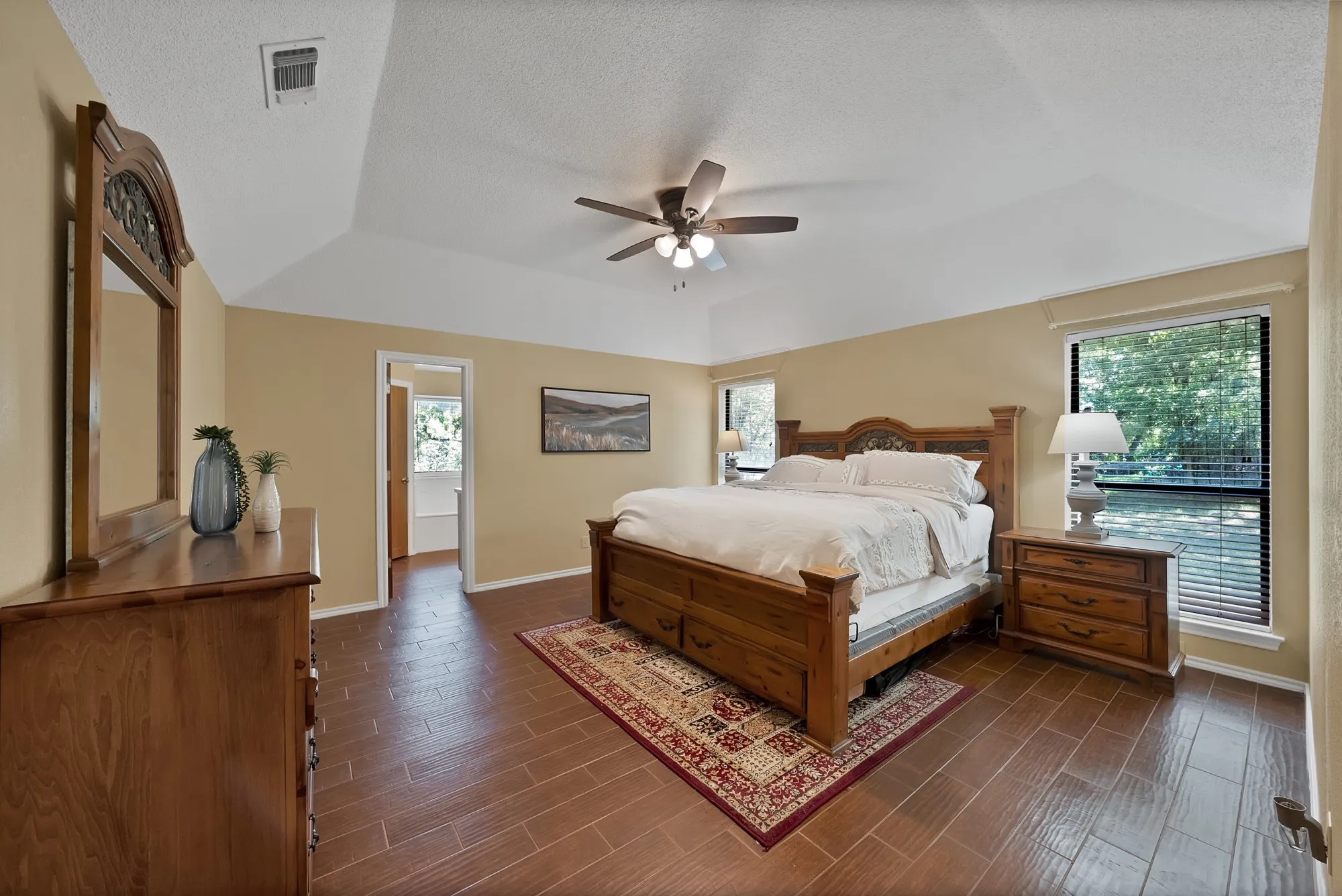 Vaulted ceiling, wood-finish flooring, ceiling fan, and multiple windows with blinds