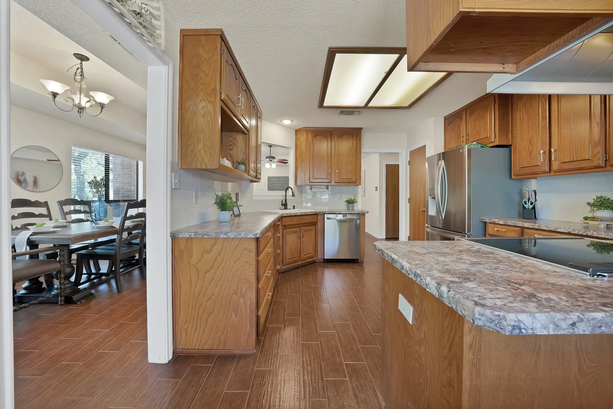 Kitchen featuring wood-finish flooring, wood cabinetry, stone-finish countertops, stainless steel appliances, and a tile backsplash