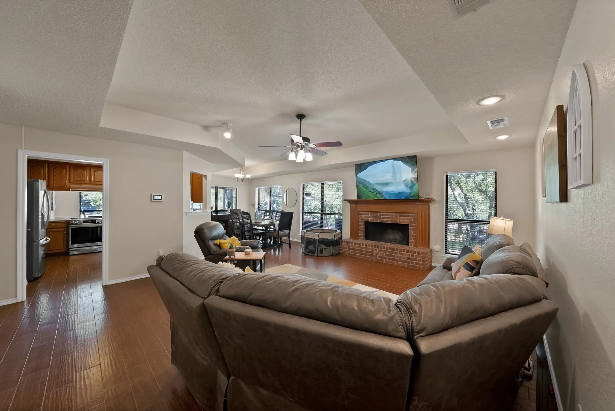Spacious living area featuring wood-finish flooring, a brick fireplace with a wood mantel, and a tray ceiling