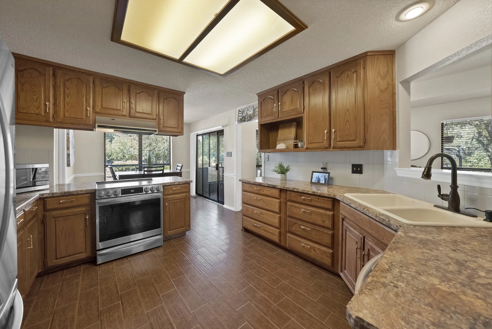 Kitchen featuring wood-finish cabinetry, stone-look countertops, stainless steel range, white subway tile backsplash, and wood-look tile flooring