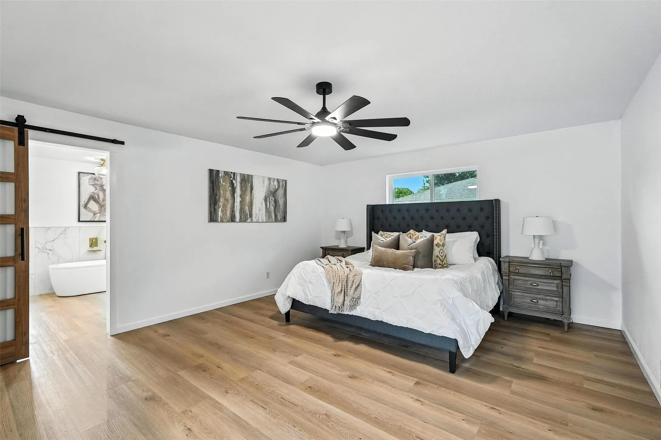 Bedroom featuring a barn door, wood finished floors, and a ceiling fan