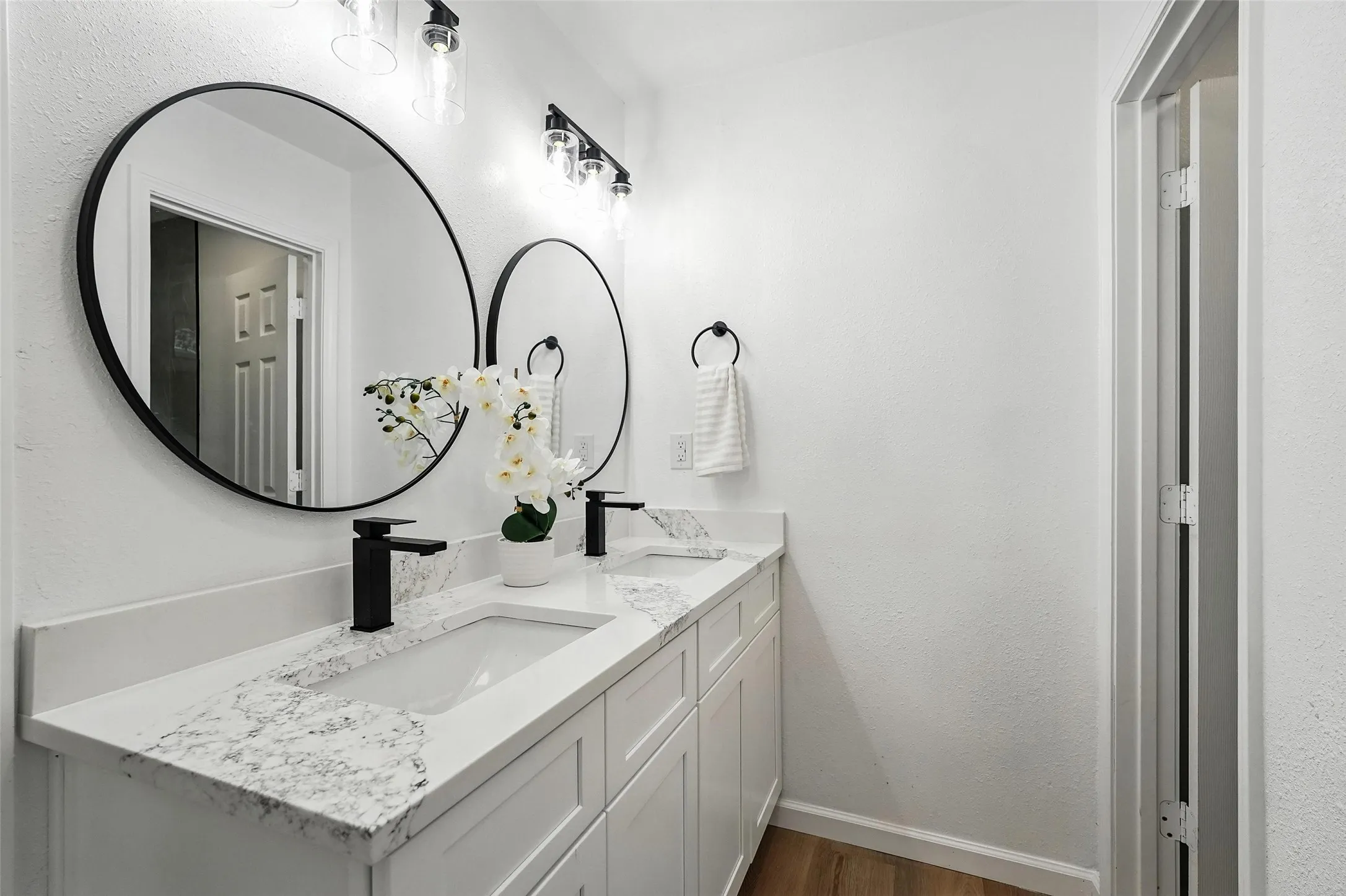 Bathroom featuring double vanity, a textured wall, and wood finished floors