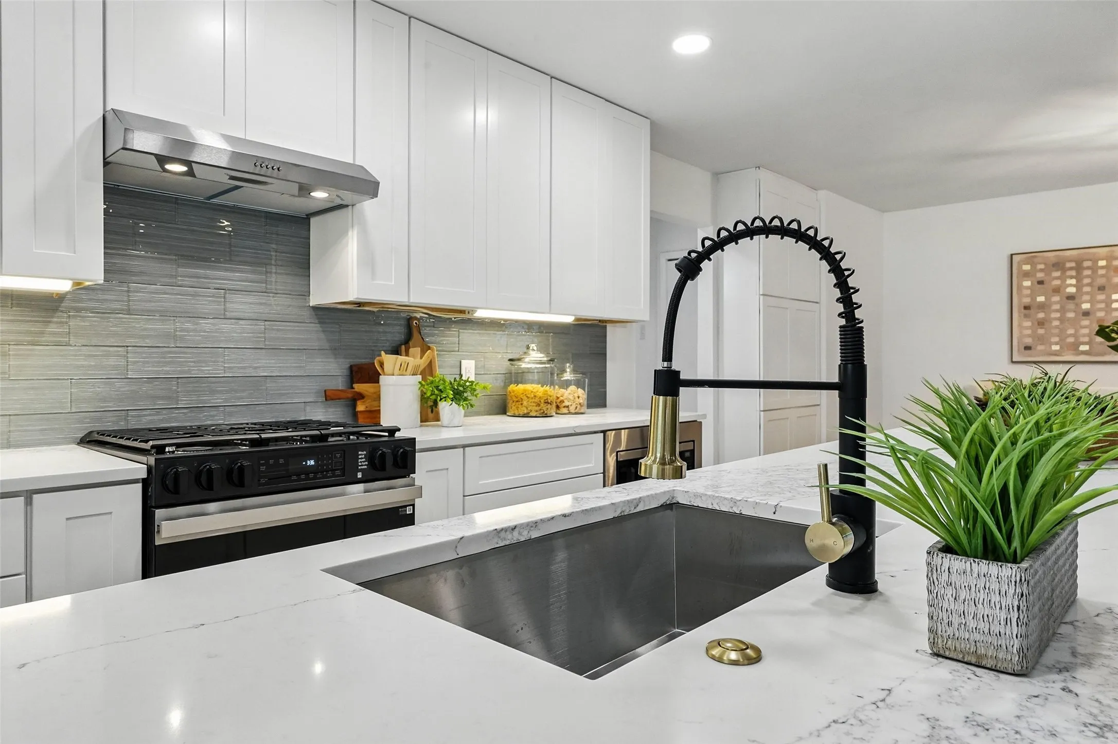 Kitchen with range with gas cooktop, range hood, white cabinetry, tasteful backsplash, and light stone counters
