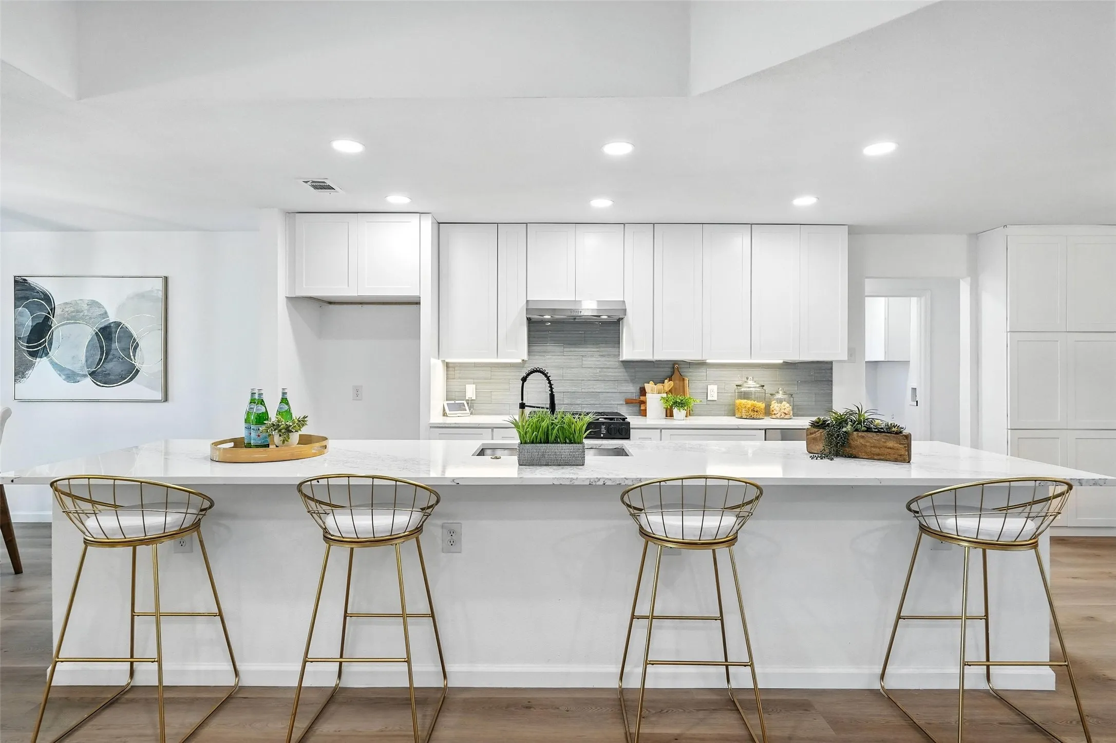 Kitchen with recessed lighting, light wood finished floors, tasteful backsplash, white cabinets, and a large island with sink