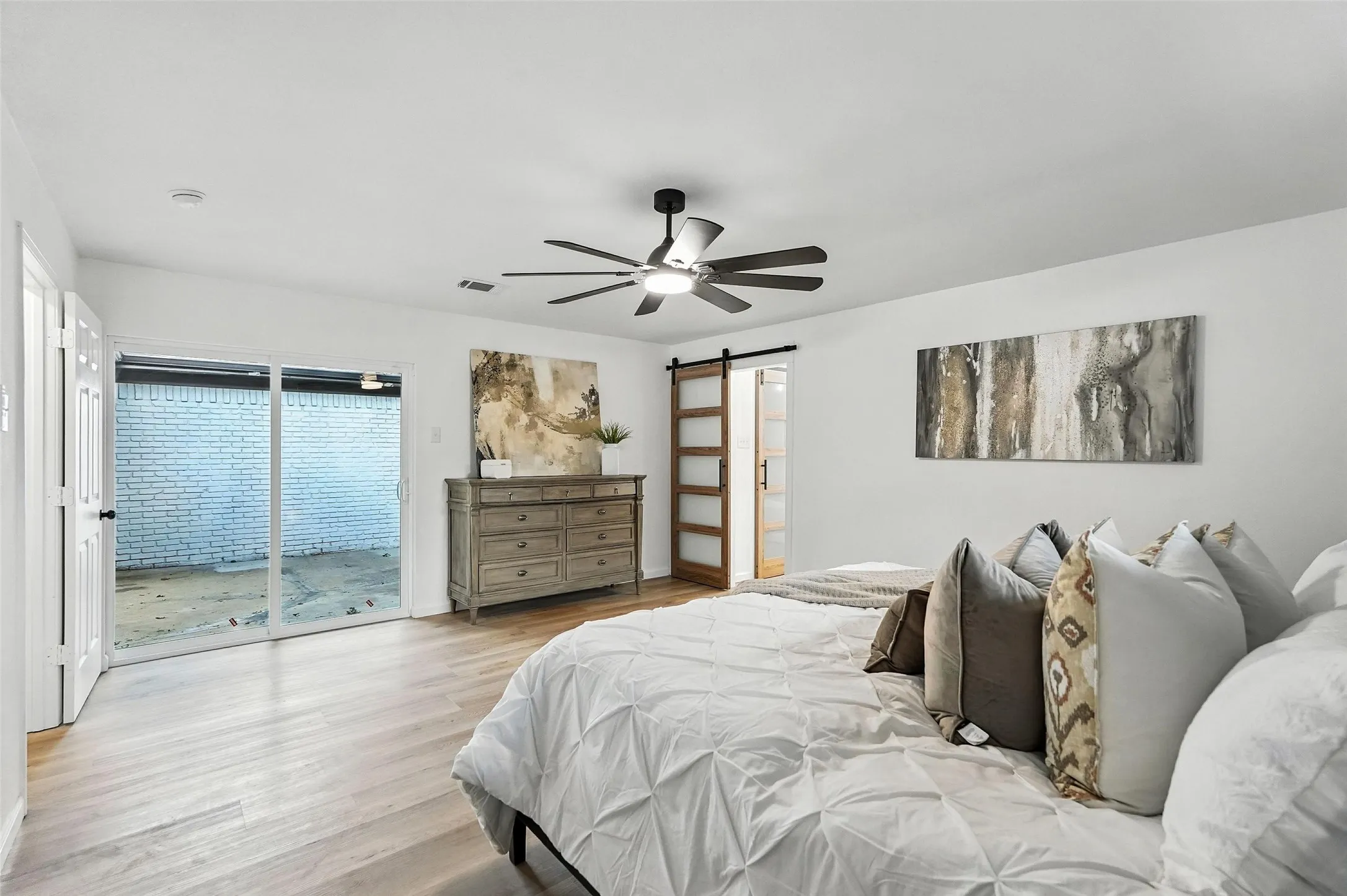 Bedroom with a barn door, access to exterior, light wood-type flooring, and a ceiling fan