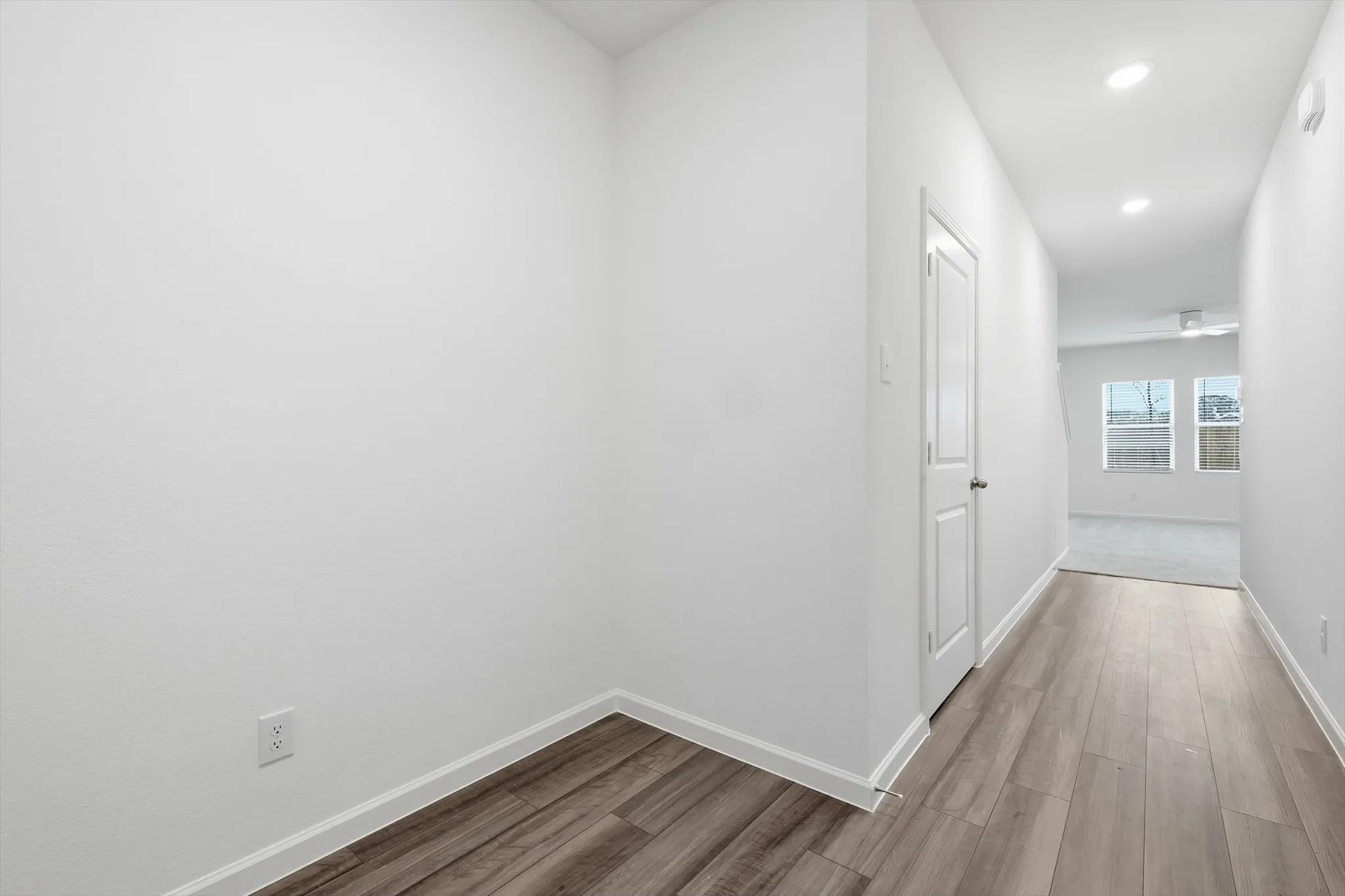 Hallway featuring wood-finish flooring, recessed lighting, and a white paneled door
