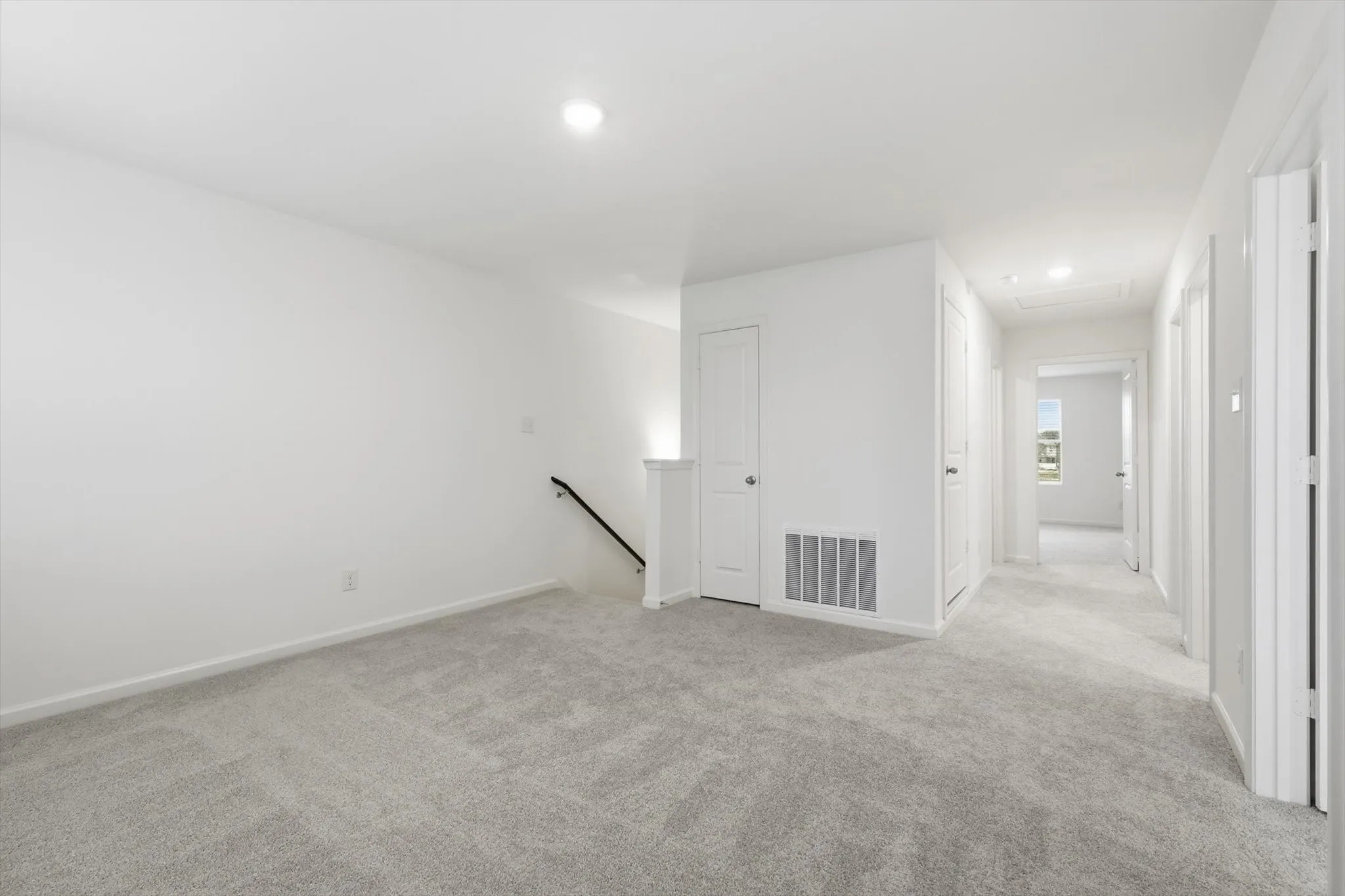 Carpeted secondary living space featuring a stairway with a black metal handrail, recessed lighting, and a neutral color palette