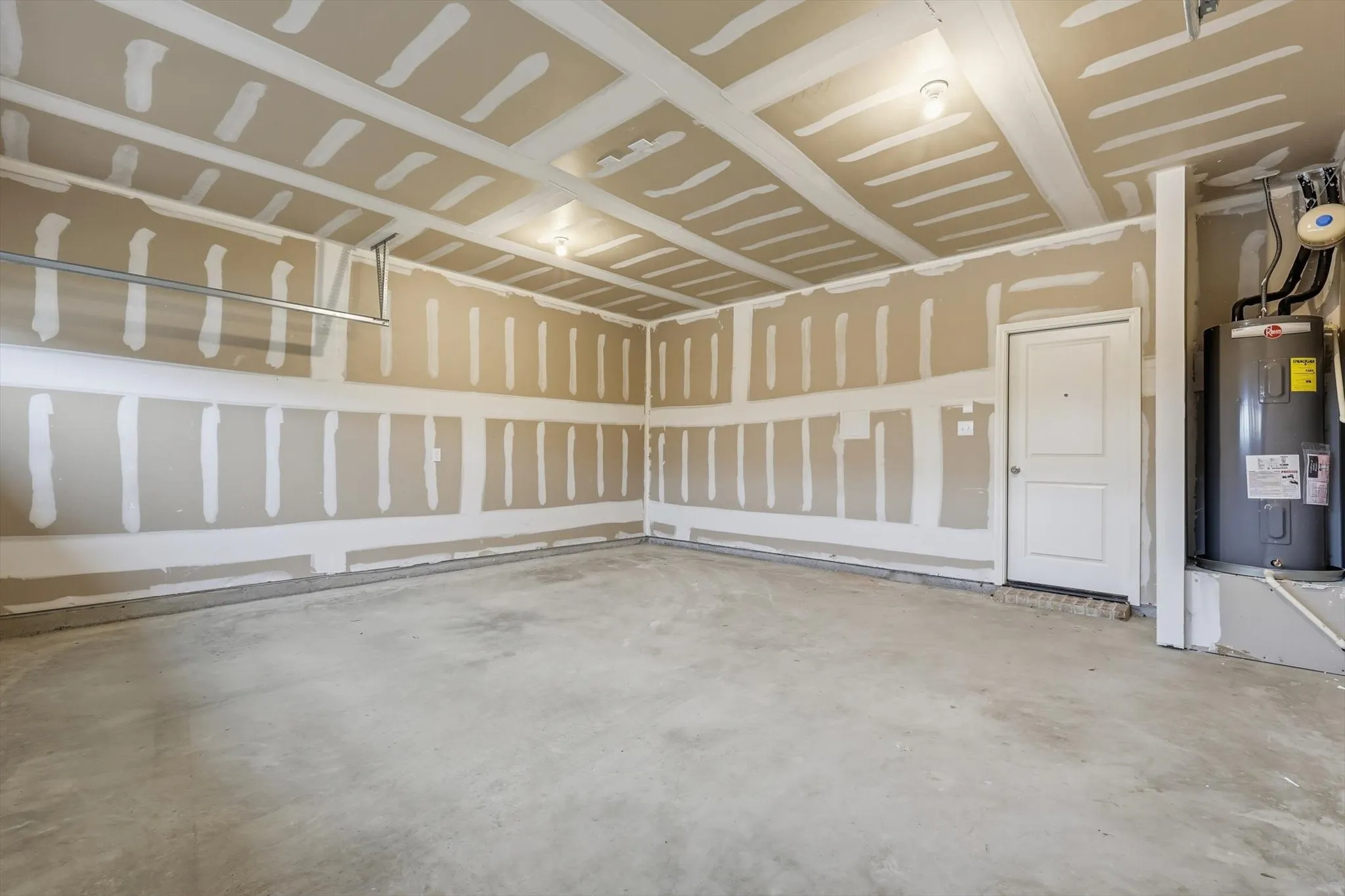 Spacious garage featuring a concrete floor, exposed drywall with taped seams, and a built-in water heater