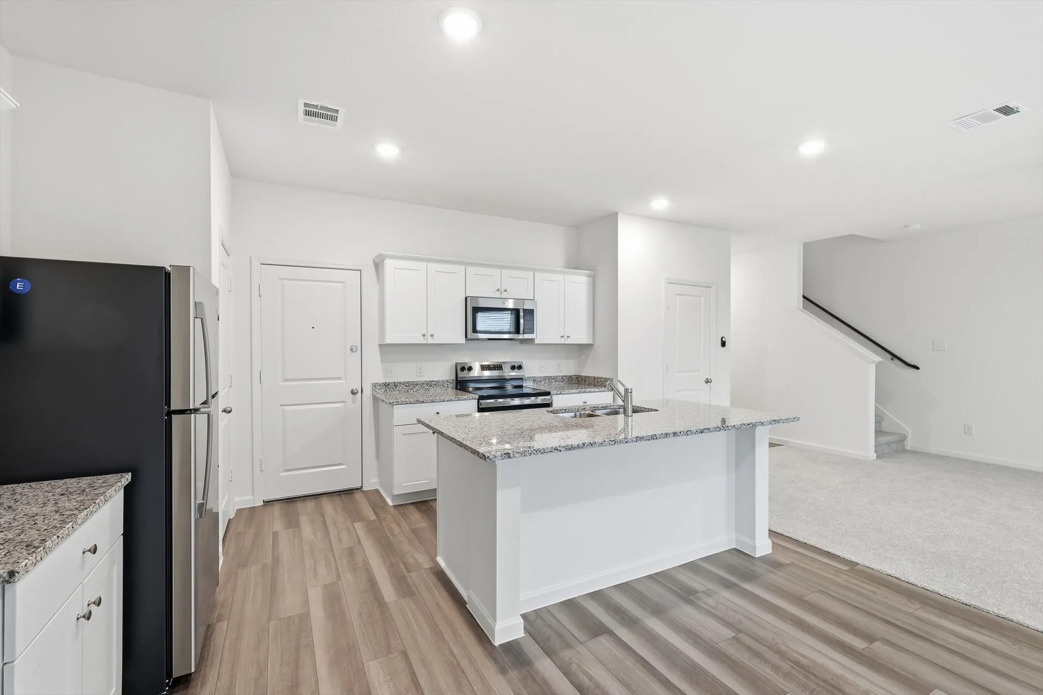 Modern kitchen featuring white cabinetry, granite countertops, wood-finish flooring, stainless steel appliances, and an island with an undermount sink