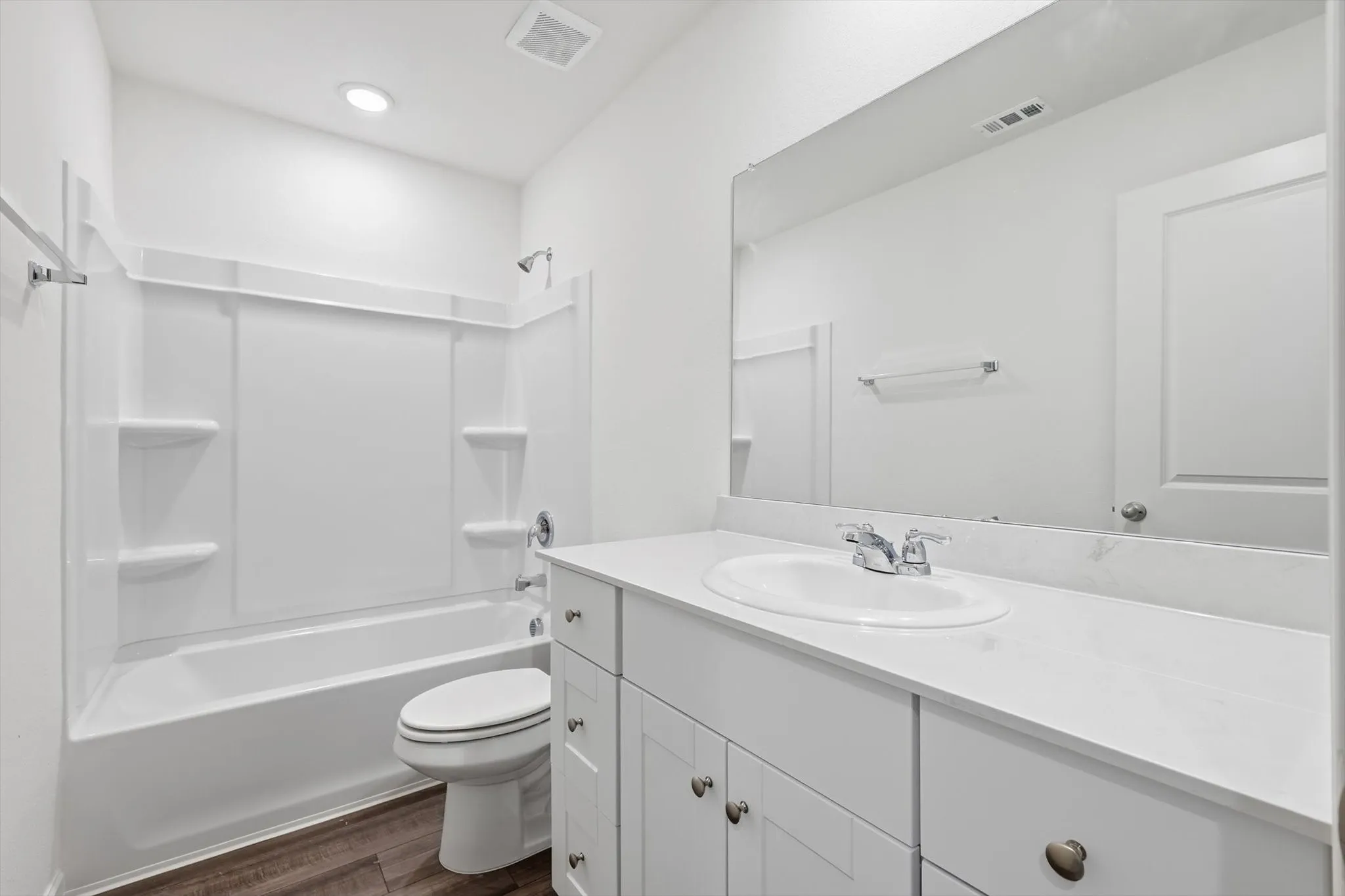 Full bathroom featuring a white tub and shower combination with integrated shelving, a white vanity with an undermount sink, chrome faucet, and a large wall-mounted mirror