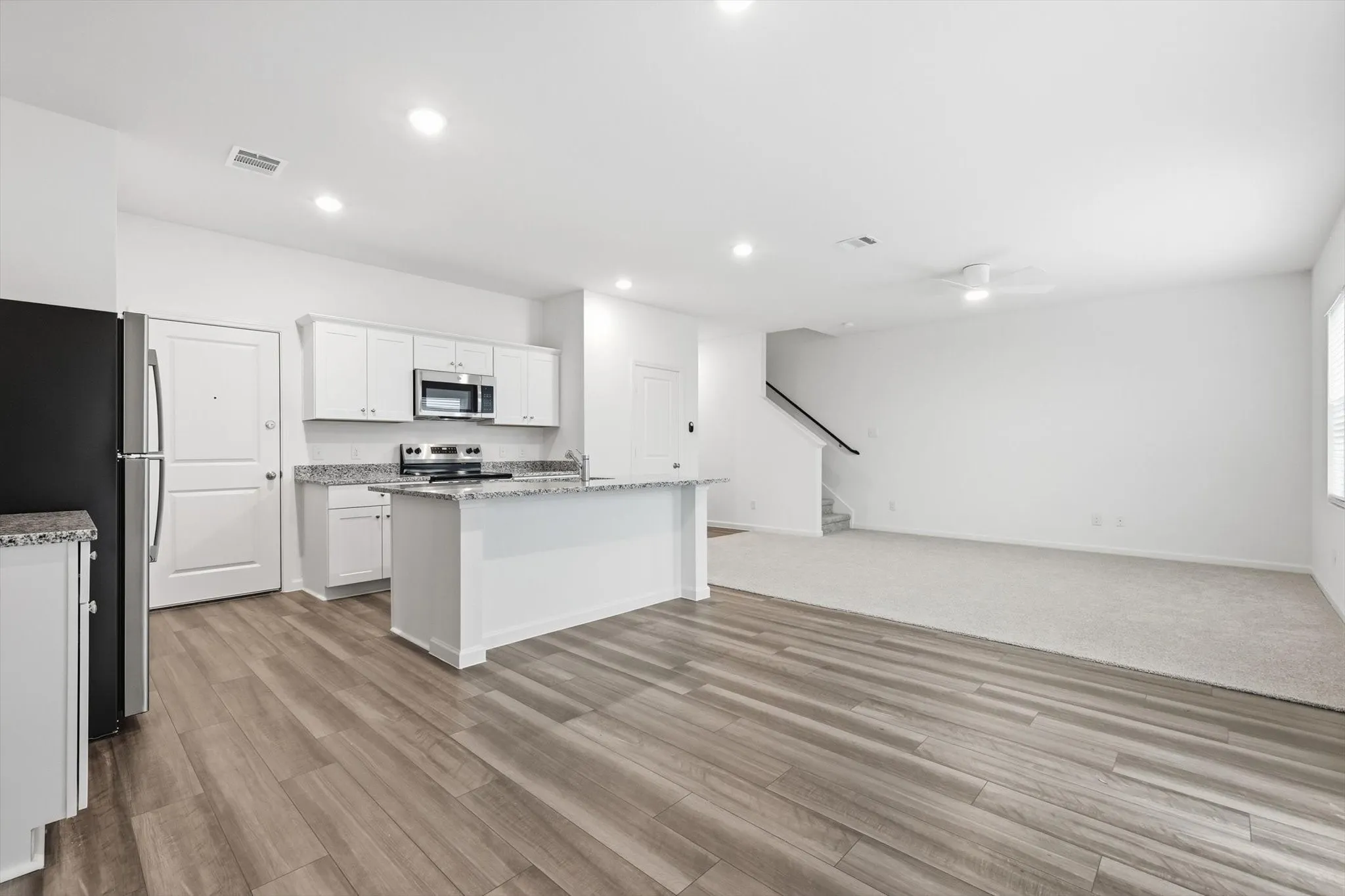 Open-concept kitchen featuring white cabinetry, granite countertops, stainless steel appliances, and wood-finish flooring