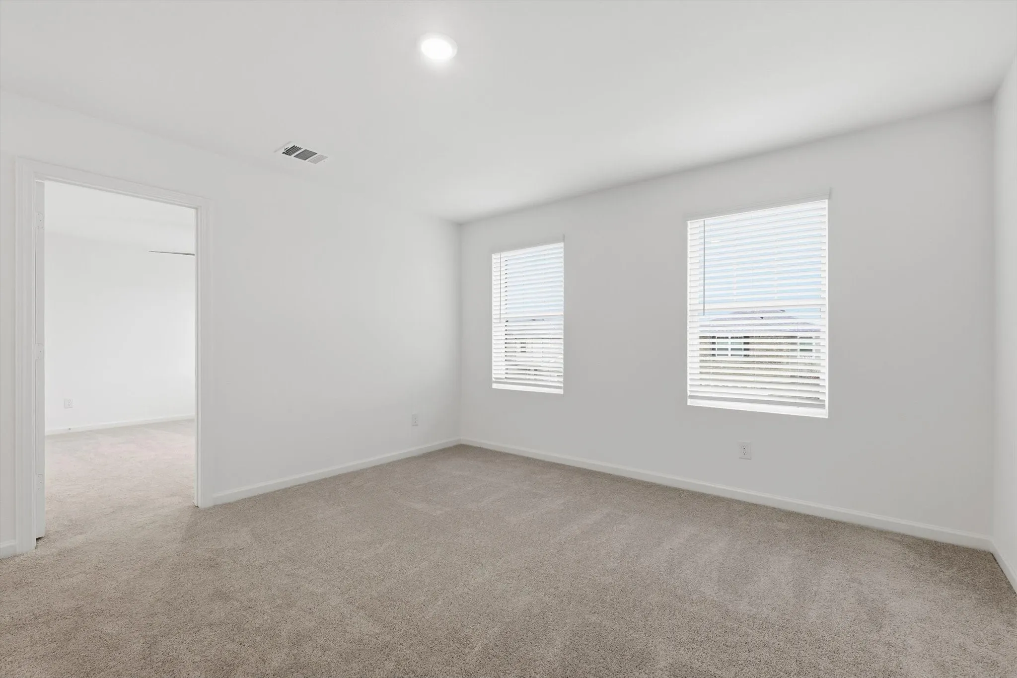Carpeted room featuring two windows with horizontal blinds, recessed ceiling lighting, and a white interior door frame